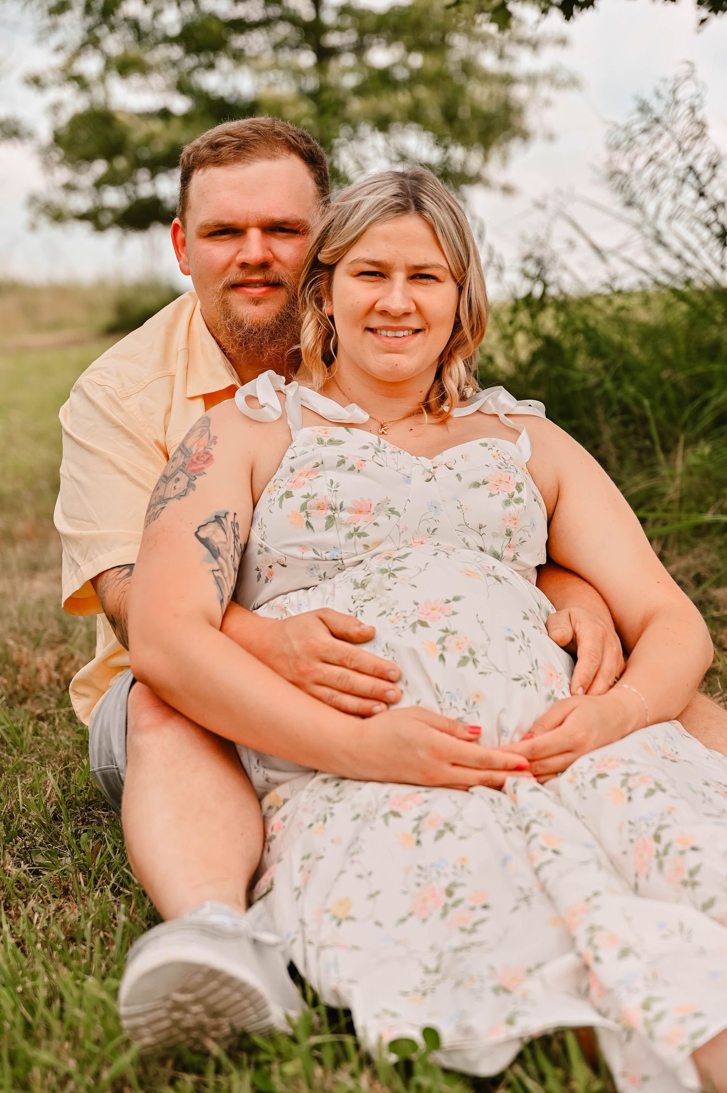 A couple poses together on grass during a maternity photoshoot.