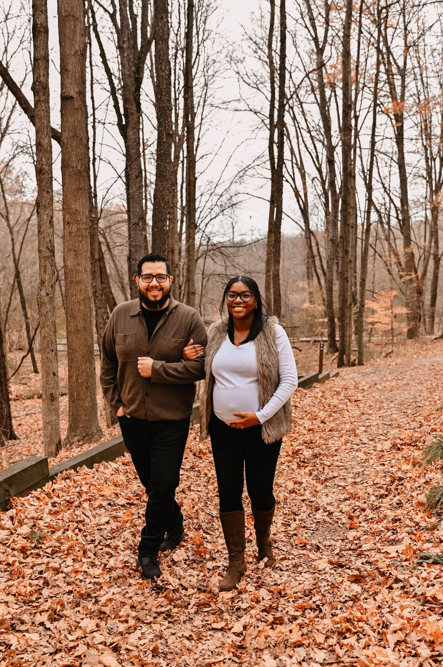 A couple walks through fallen autumn leaves on a forest trail.