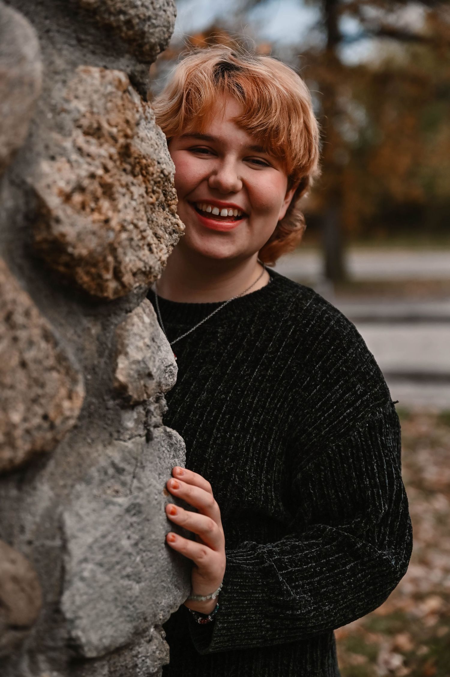 A series of outdoor portraits against a stone wall showing a black knit sweater in autumn.