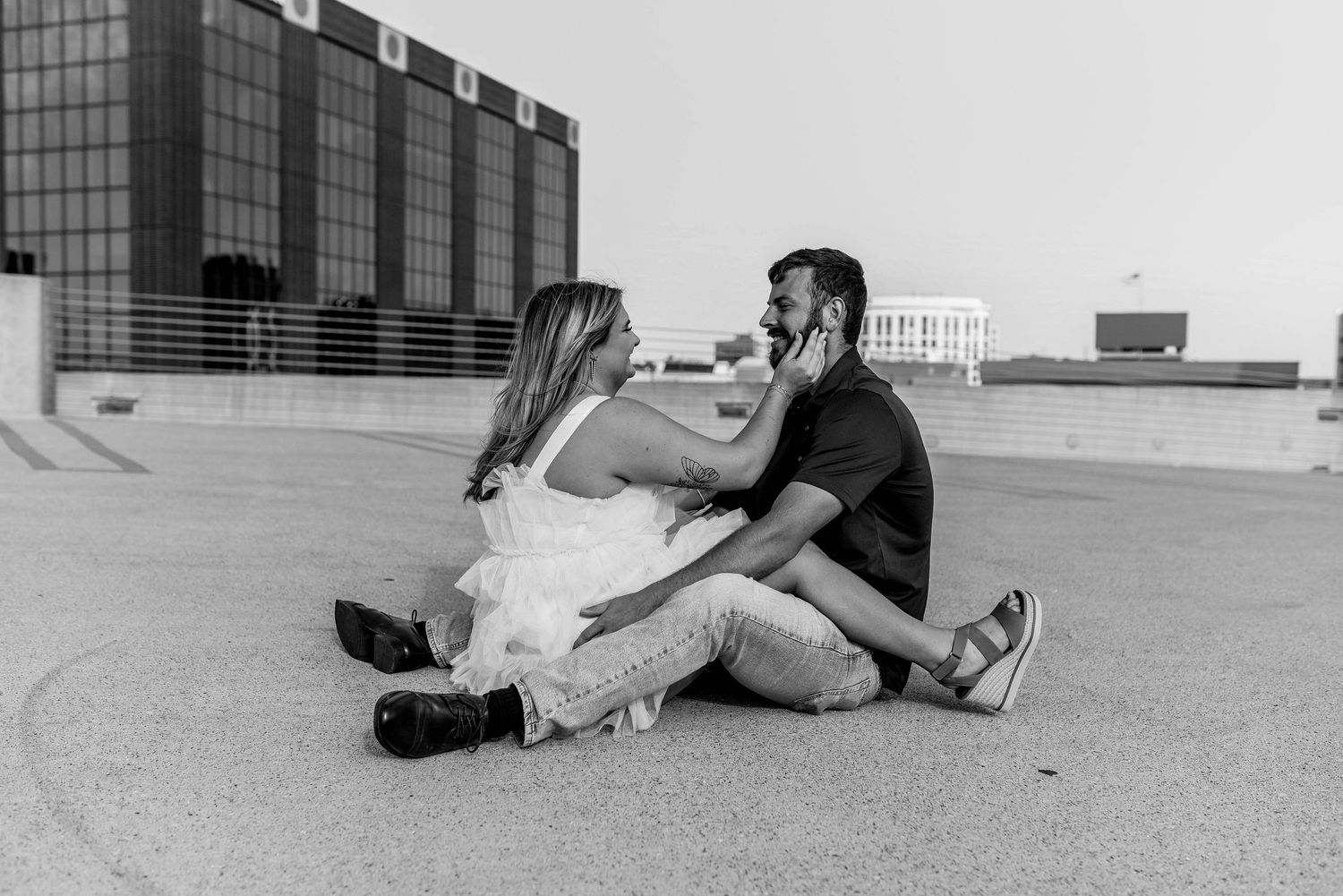 A couple relaxes together on a concrete surface in black and white photography.
