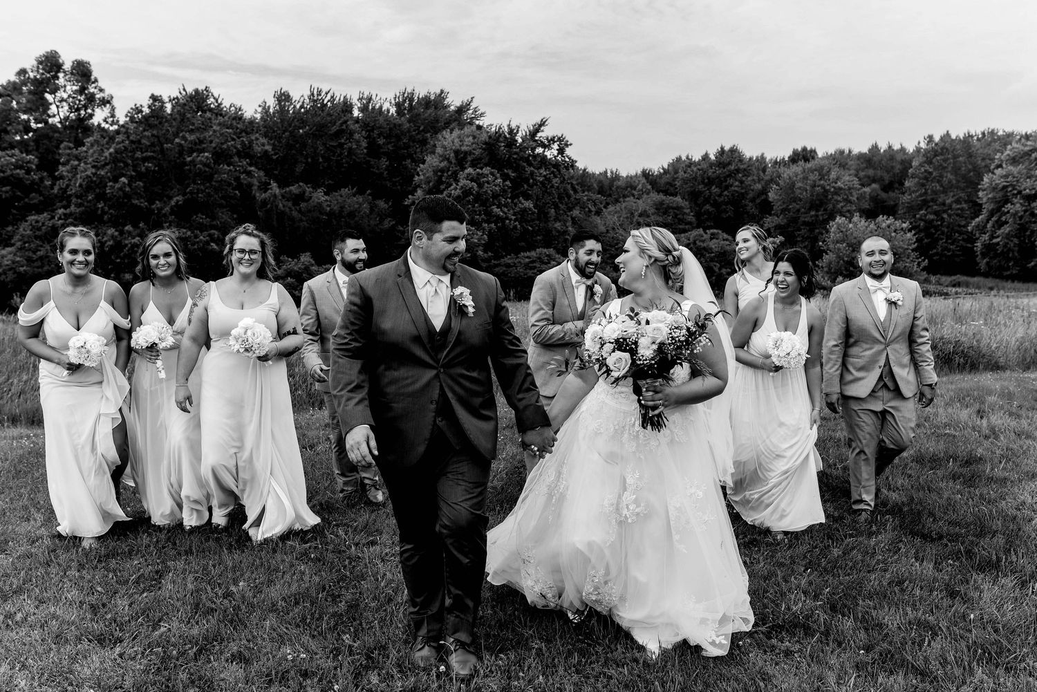 Black and white photo of wedding party walking and laughing together in a field.