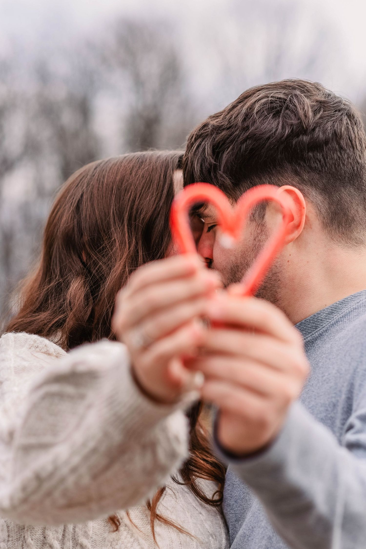 Couple making heart shape with hands against winter sky.