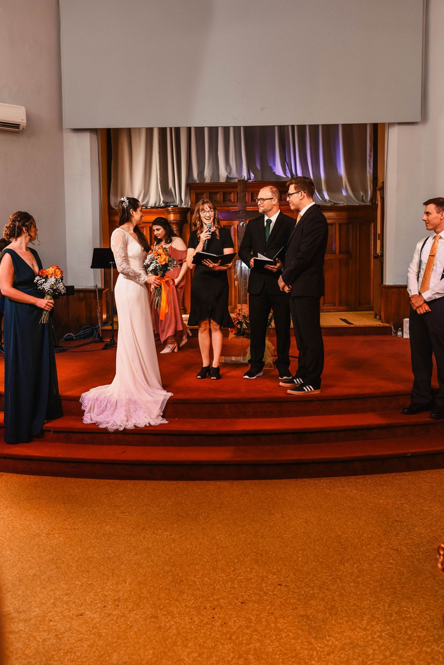 Wedding party performs choreographed dance routine on stage in formal attire.