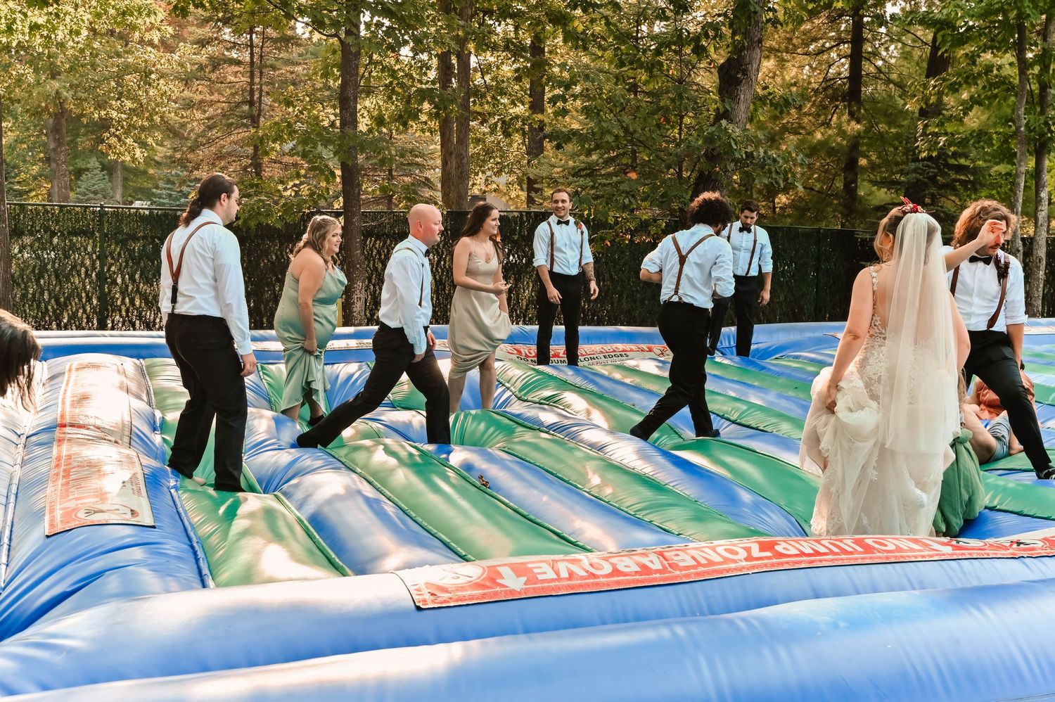 Wedding party jumping and playing on a colorful bounce house at an outdoor reception.