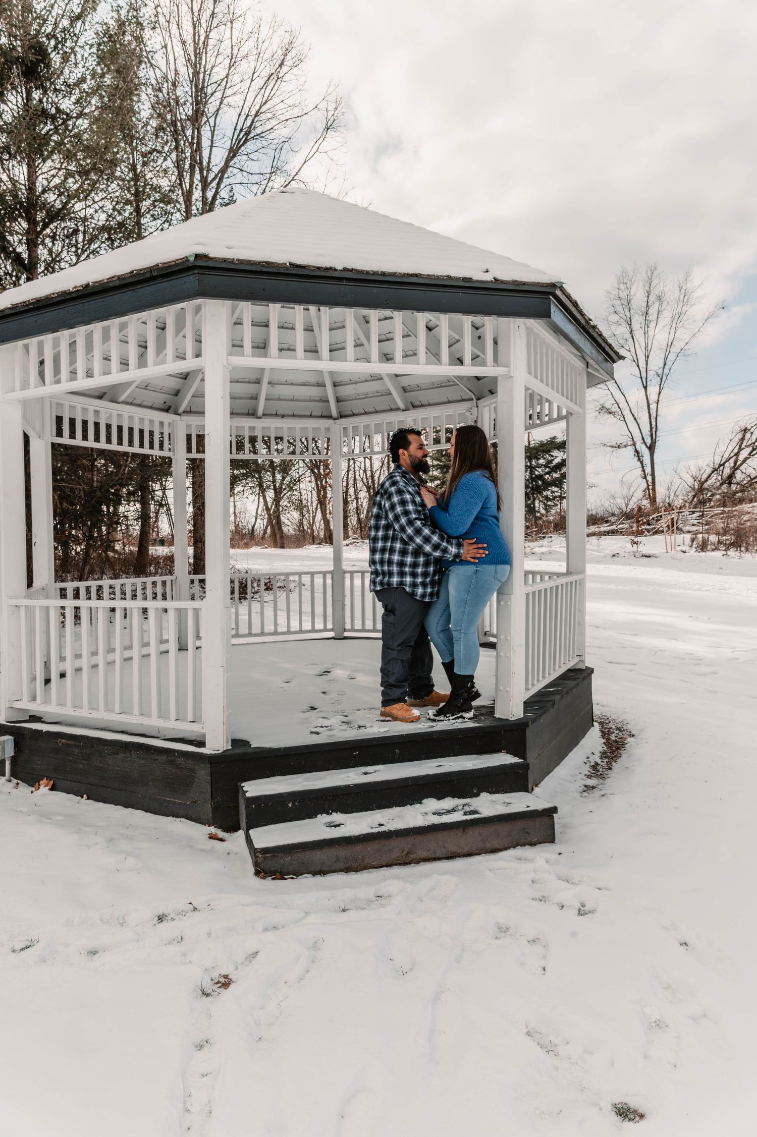 Winter engagement photos in white gazebo surrounded by snow.