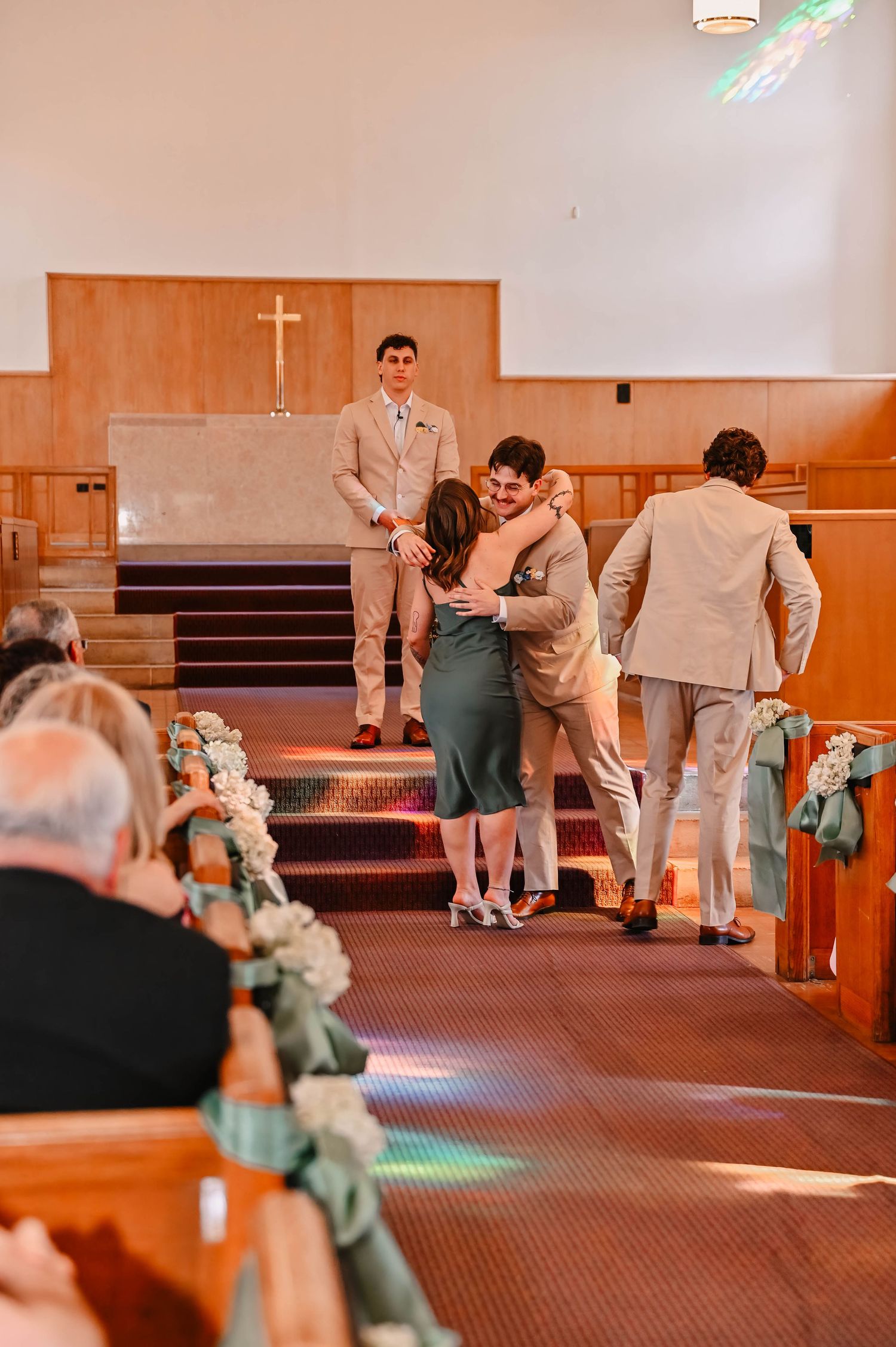 Wedding ceremony taking place in a church with wooden pews and decorative floral arrangements.