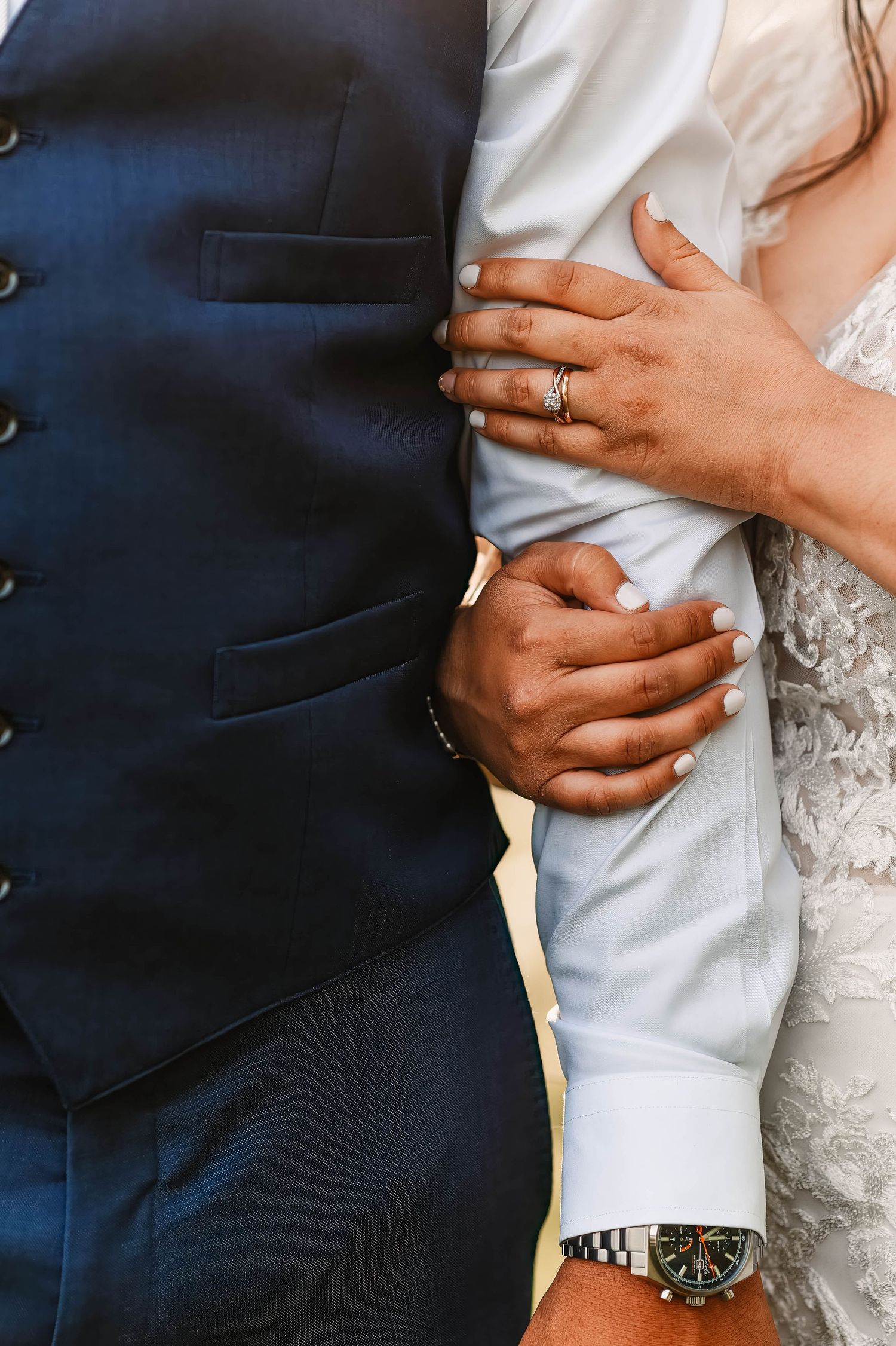 Close-up details of wedding attire showing hands embracing and a white lace dress against a navy suit.