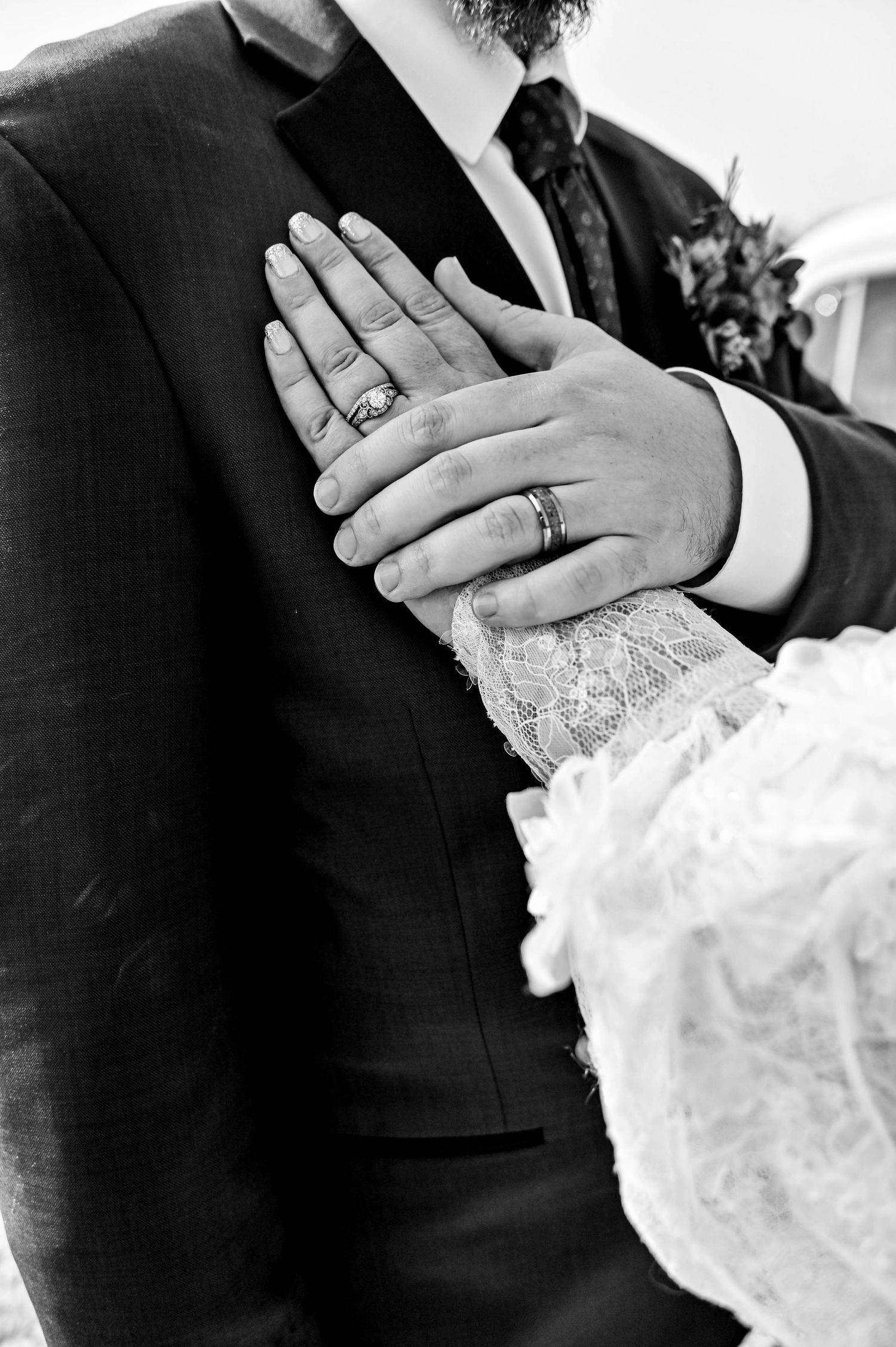 Close-up black and white photo of wedding rings and lace dress details.