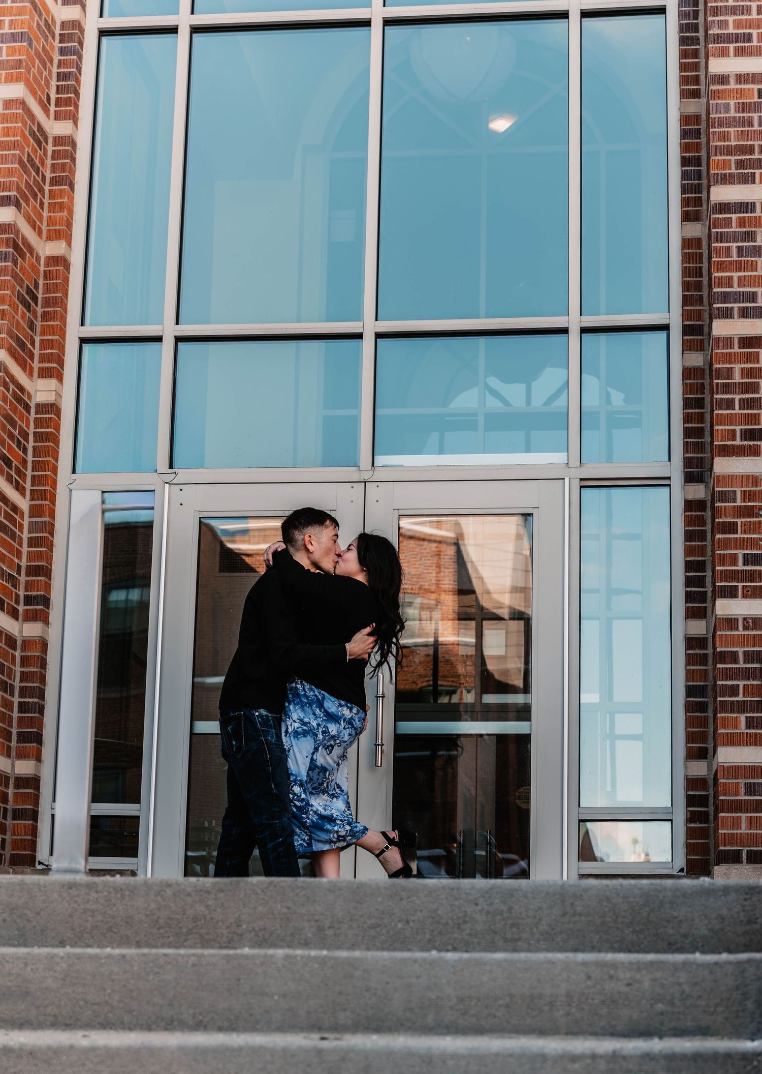Sequence of couple by glass windows of modern brick building.