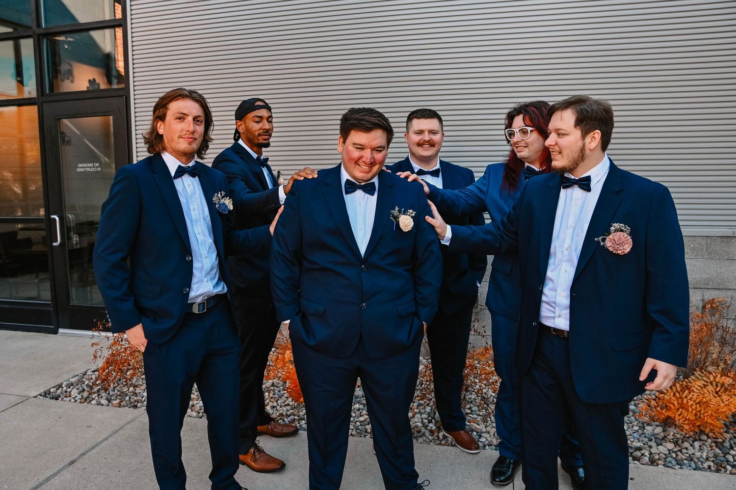 Groomsmen in navy suits and bow ties share a candid moment outside.