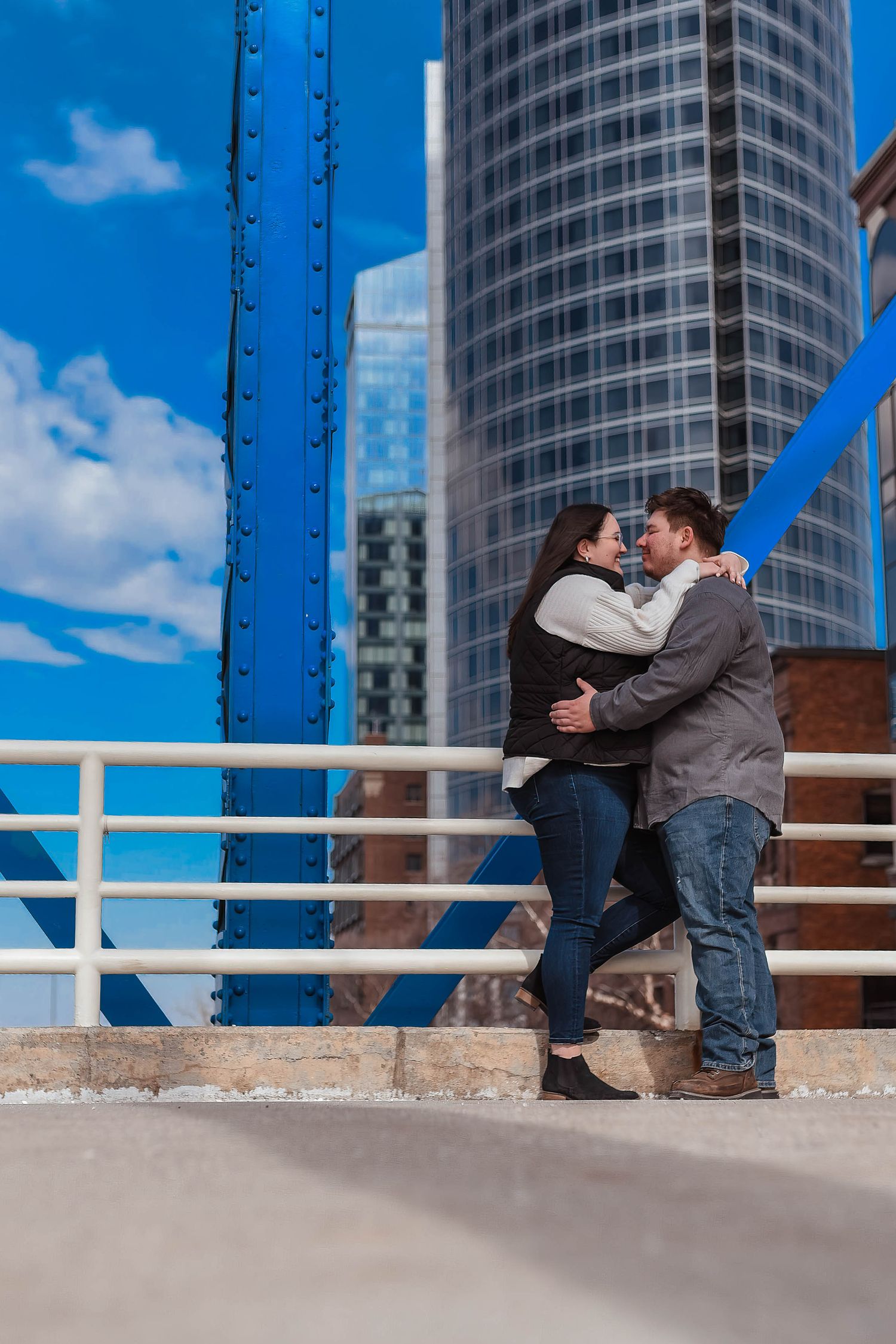 Couple sharing romantic moment on bridge with modern city buildings in background.