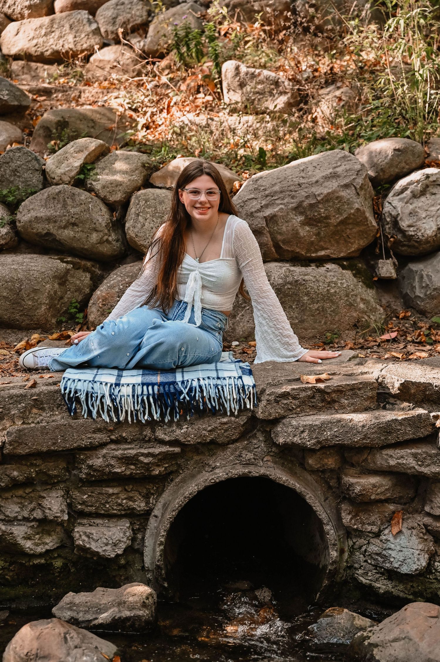 Person relaxes on stone wall near dark cave entrance during autumn season.