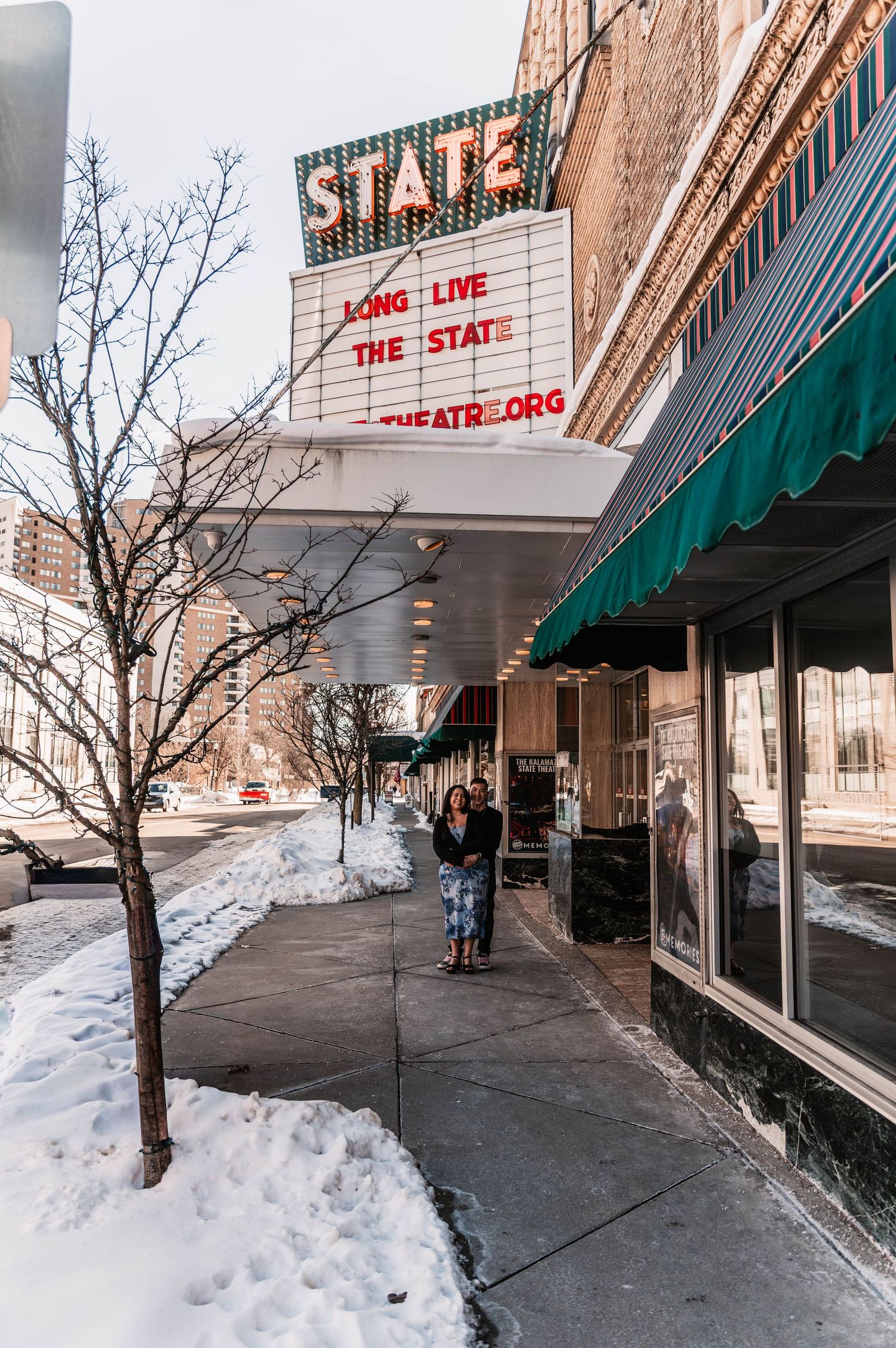 Snow-covered sidewalk outside The State theater with green awnings in winter.