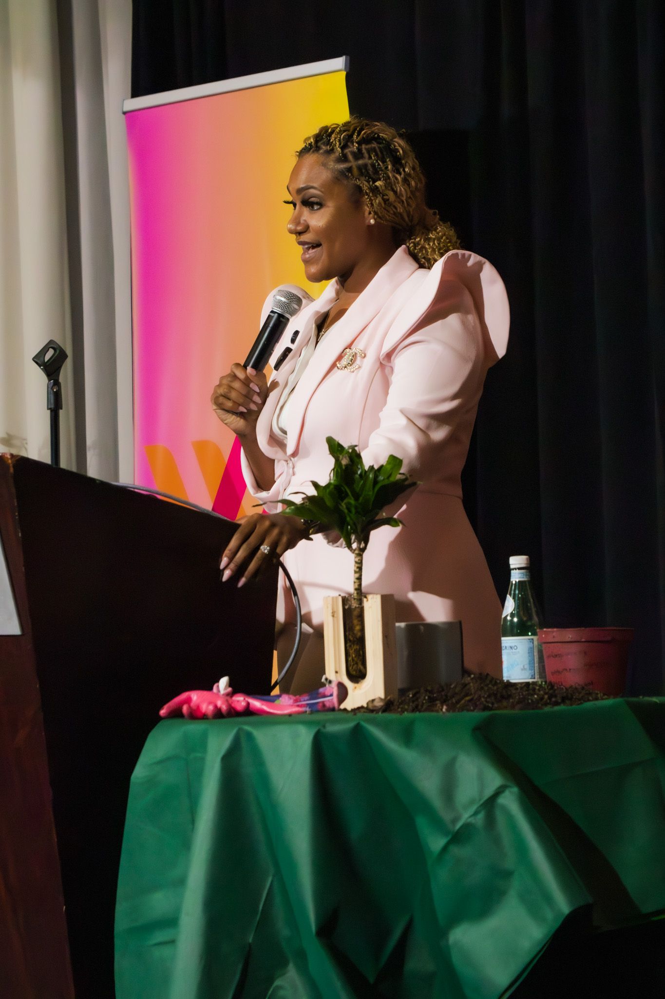 Presenter speaks at podium with green tablecloth and colorful backdrop.