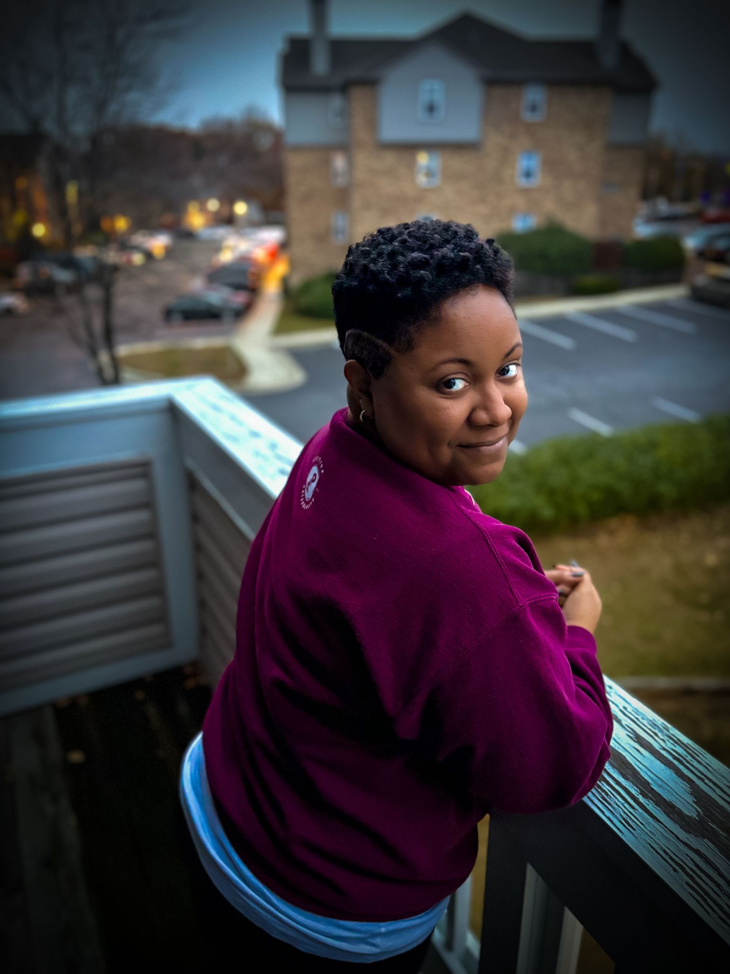 Person in purple sweater sitting on blue bench outdoors during evening light.