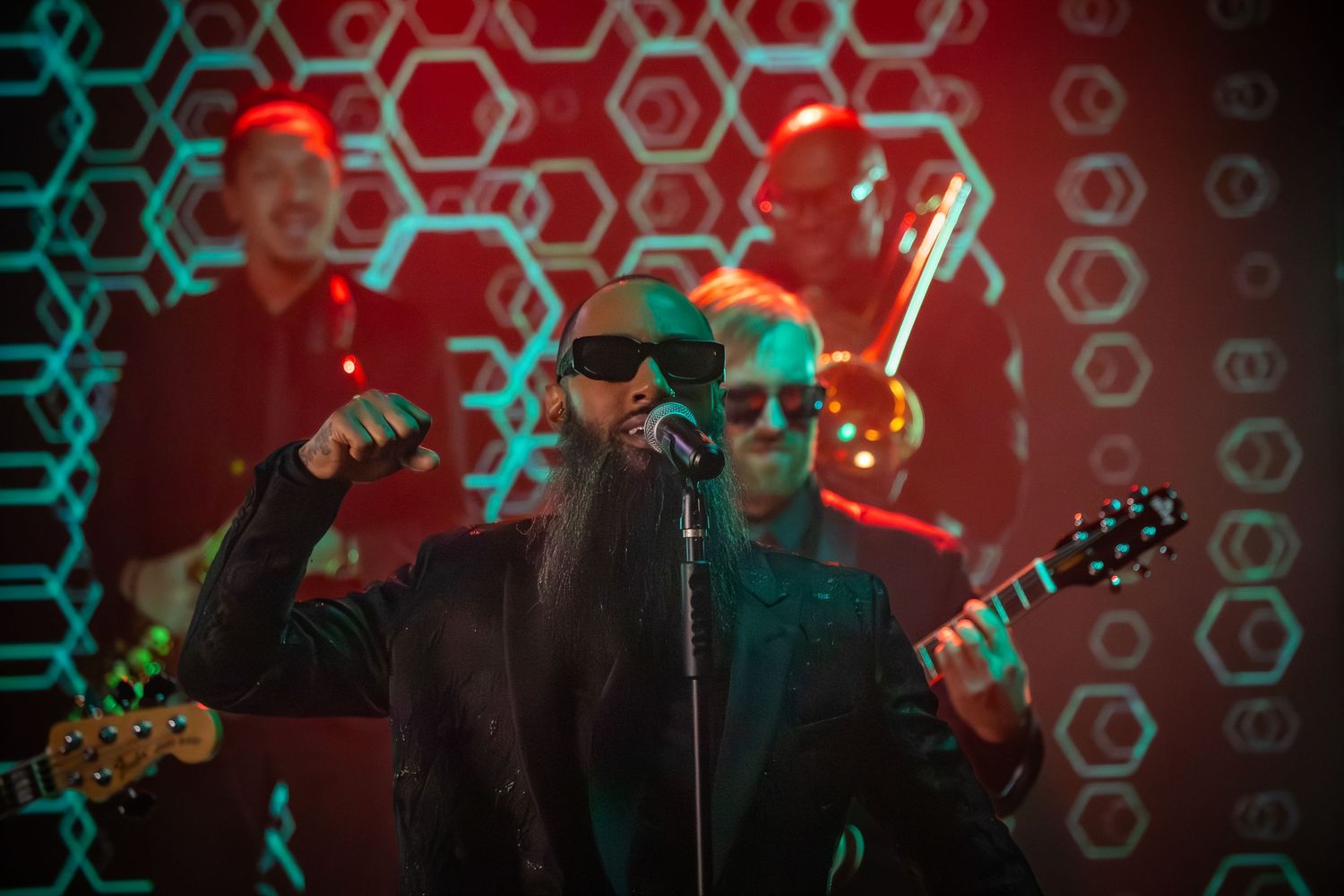 Band performs on stage with red and teal hexagonal pattern backdrop.
