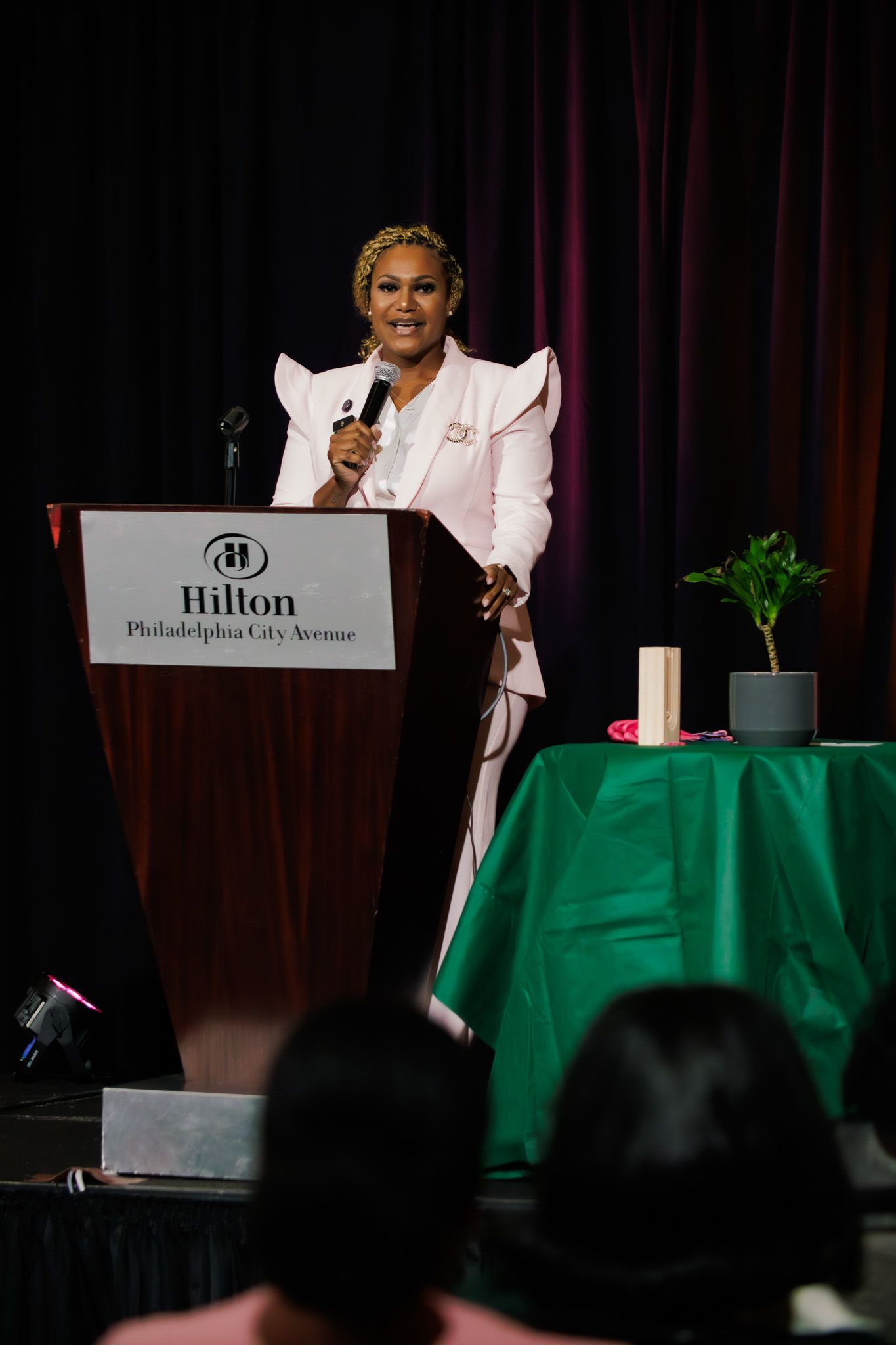 Conference speaker presents at Hilton hotel podium with dramatic lighting.