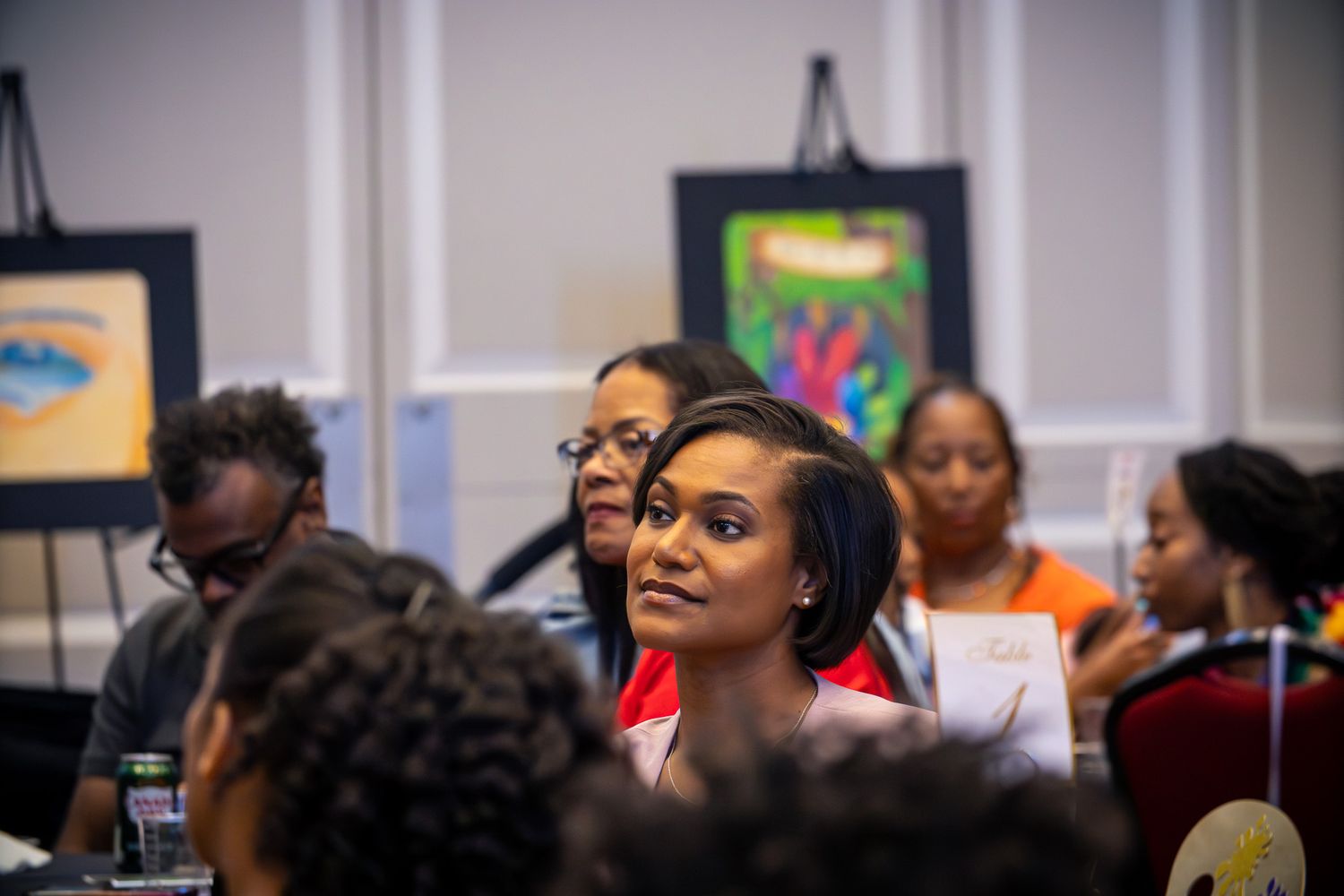 Diverse group of people attentively listening at an indoor seminar with colorful artwork displayed in the background.