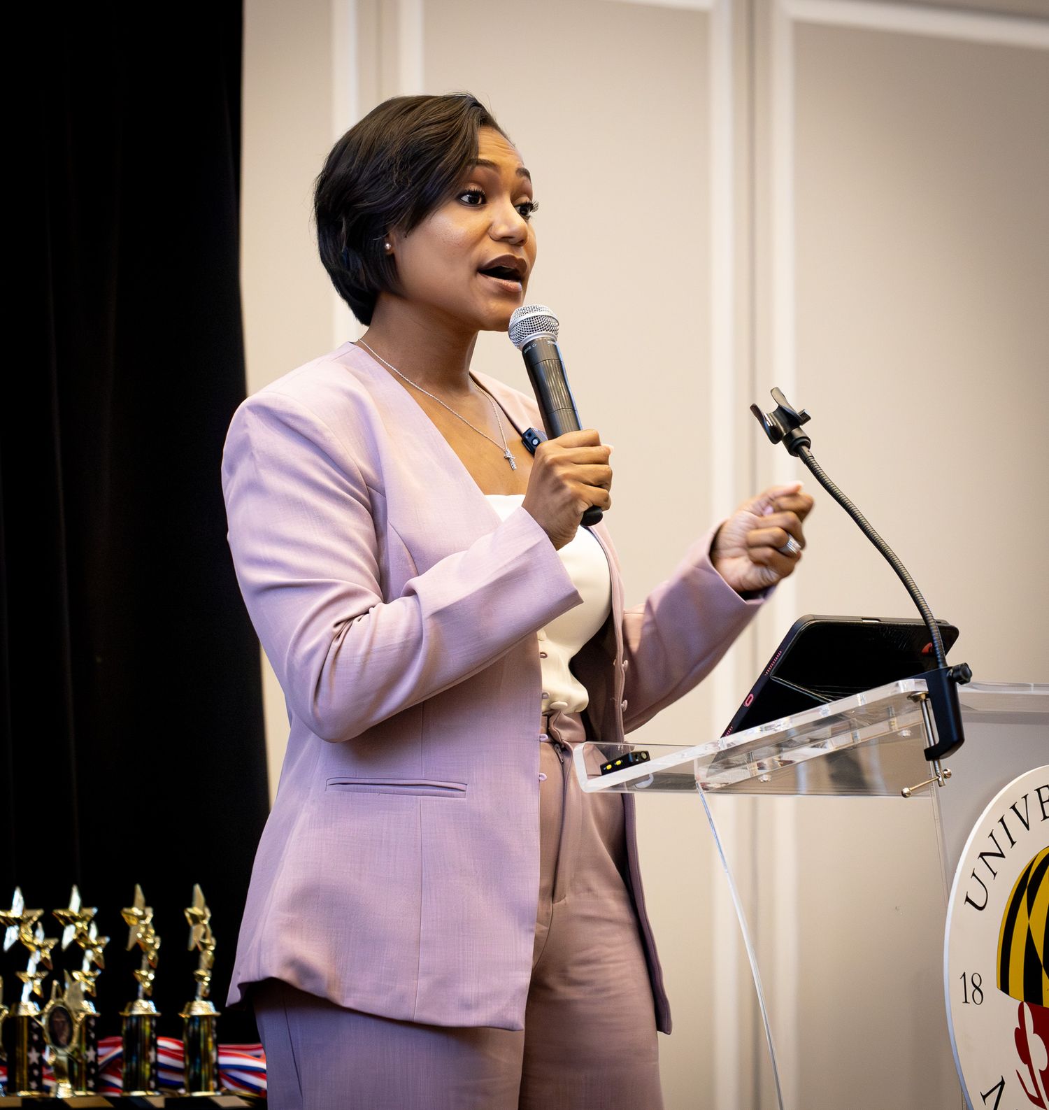 Woman in pink blazer speaking at university podium with microphone at formal awards ceremony.