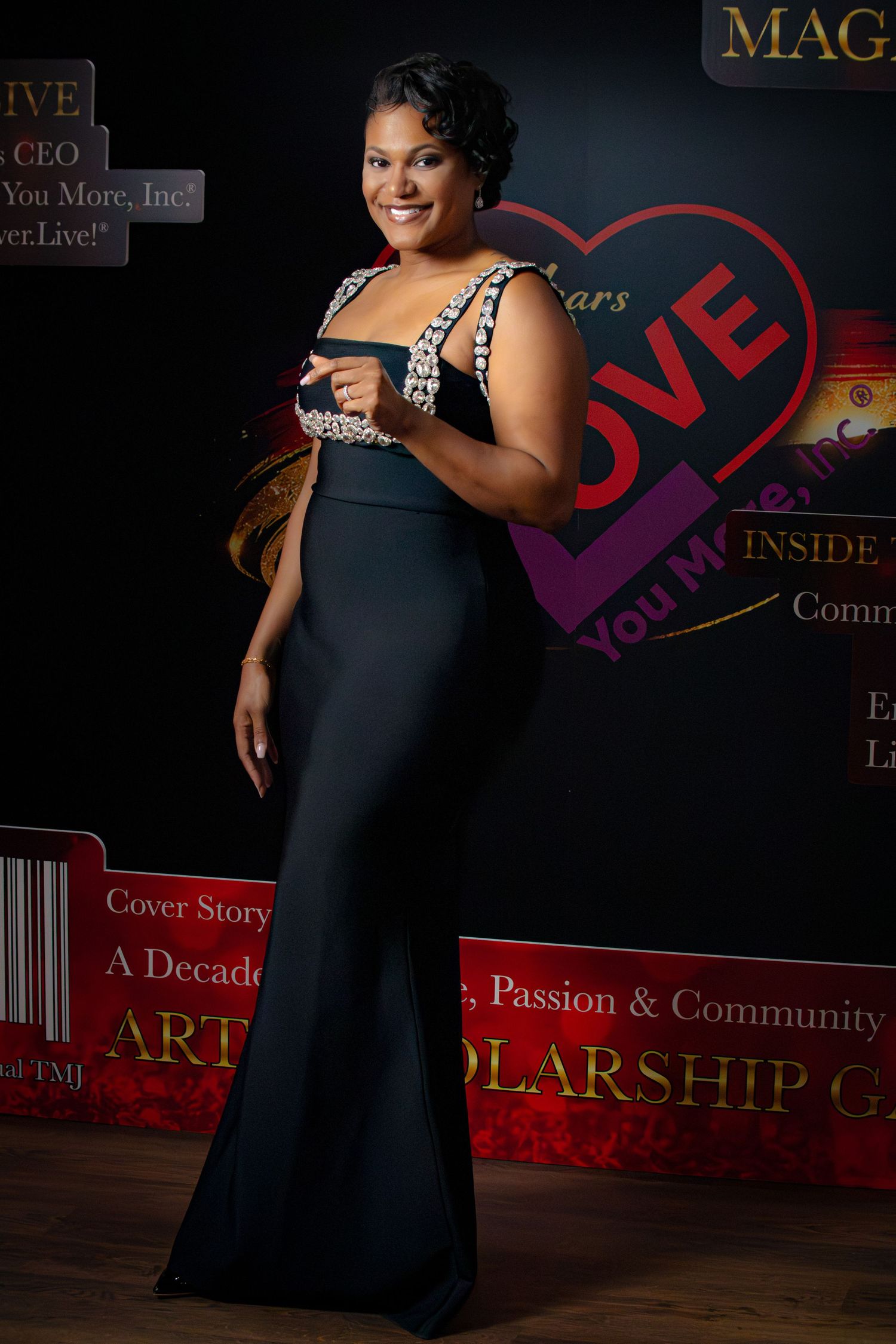 A woman in a black formal dress poses against a dark backdrop with illuminated red signage and magazine-style decor.