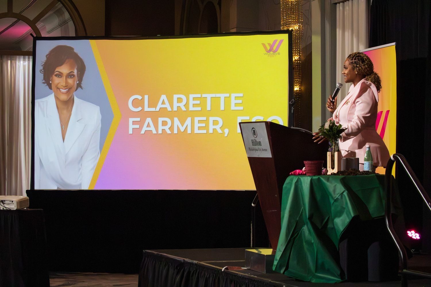 Event speaker delivers presentation with vibrant digital display backdrop.