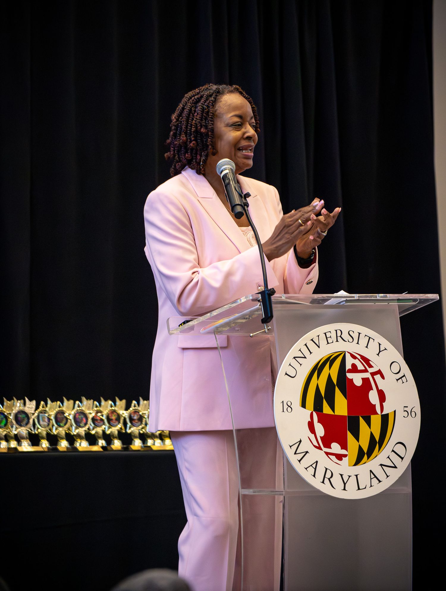 Woman in pink suit speaking at University of Maryland podium during formal event.