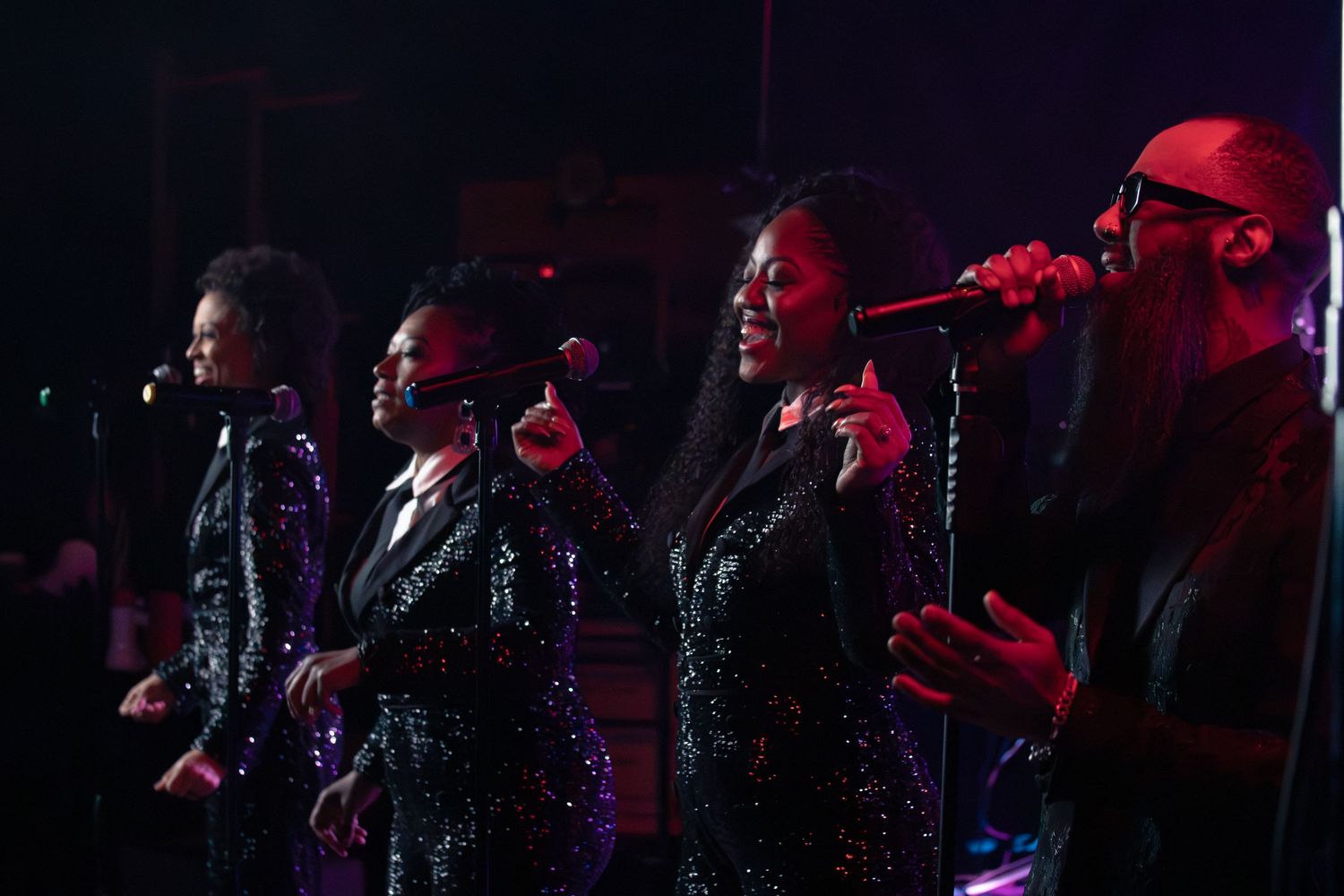 Musicians in dark silhouettes perform against dramatic red stage lighting.