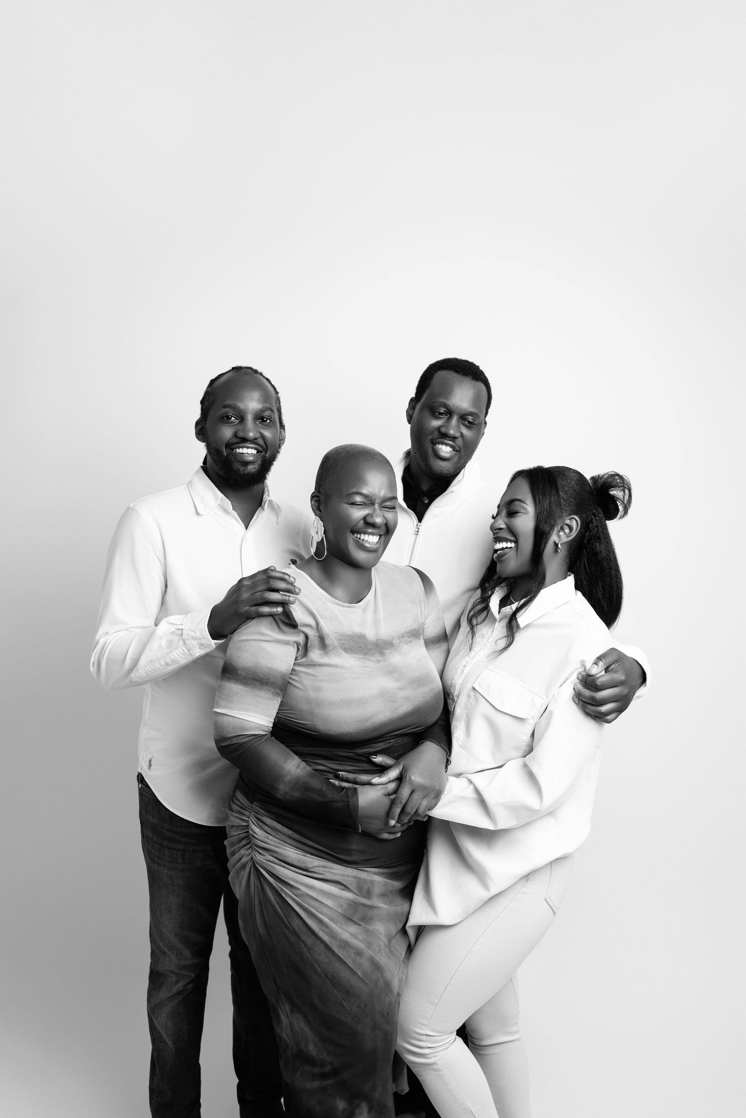 Three people in black and white wearing casual clothing laugh and embrace while posing together for a joyful portrait series.