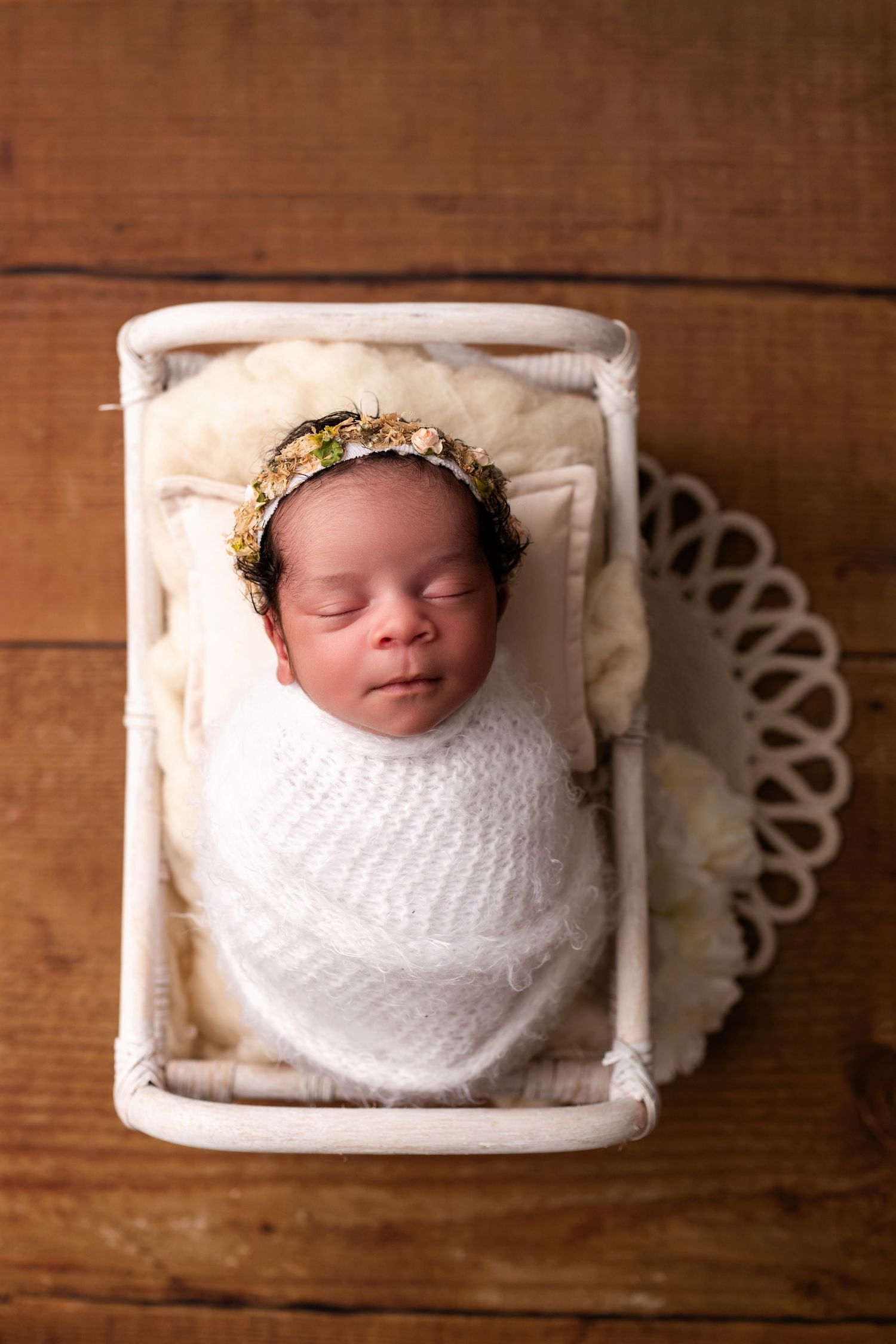 Sleeping newborn wearing crown posed in white basket on wooden background.