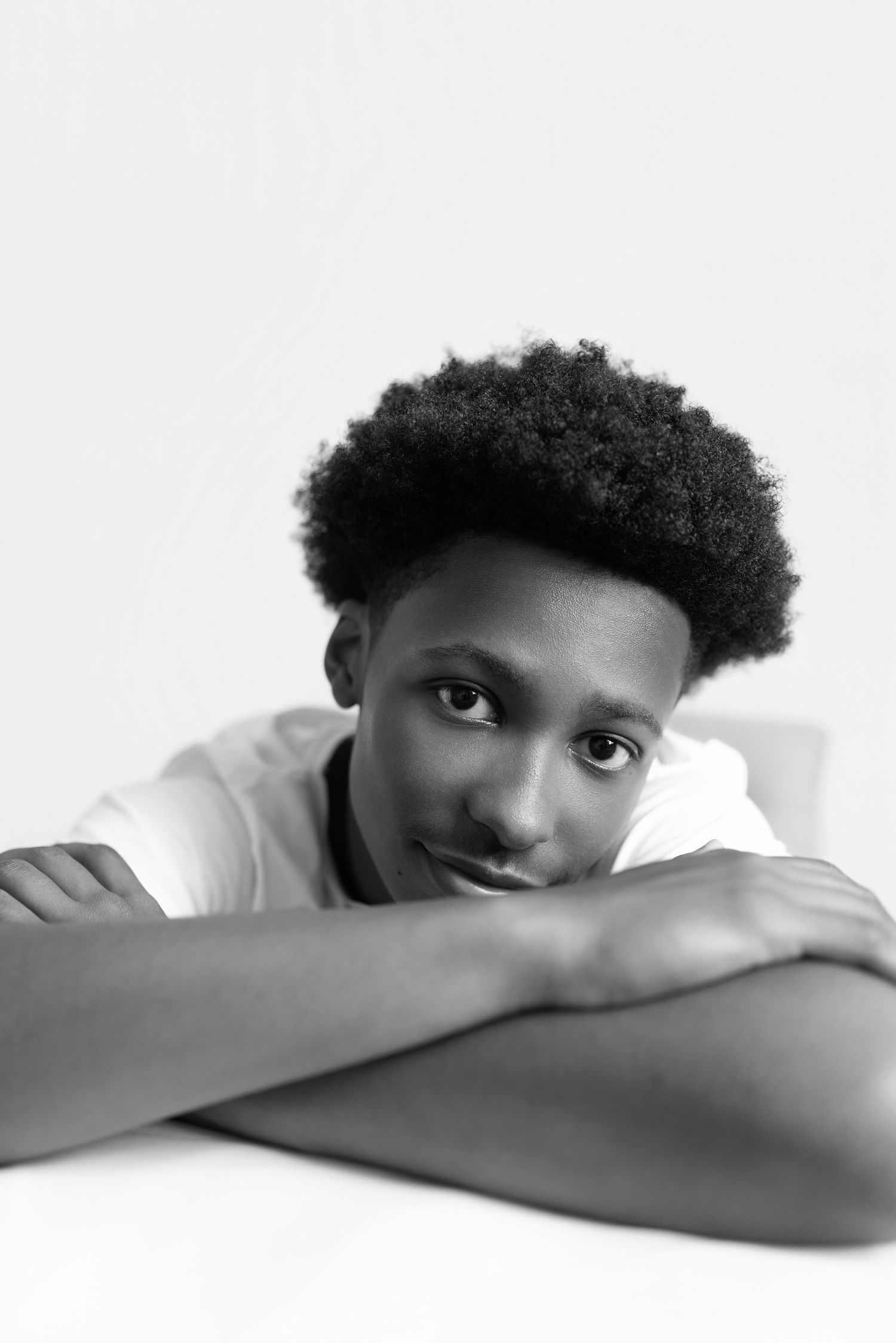 Black and white portrait of a young man with an afro hairstyle resting his chin on crossed arms.