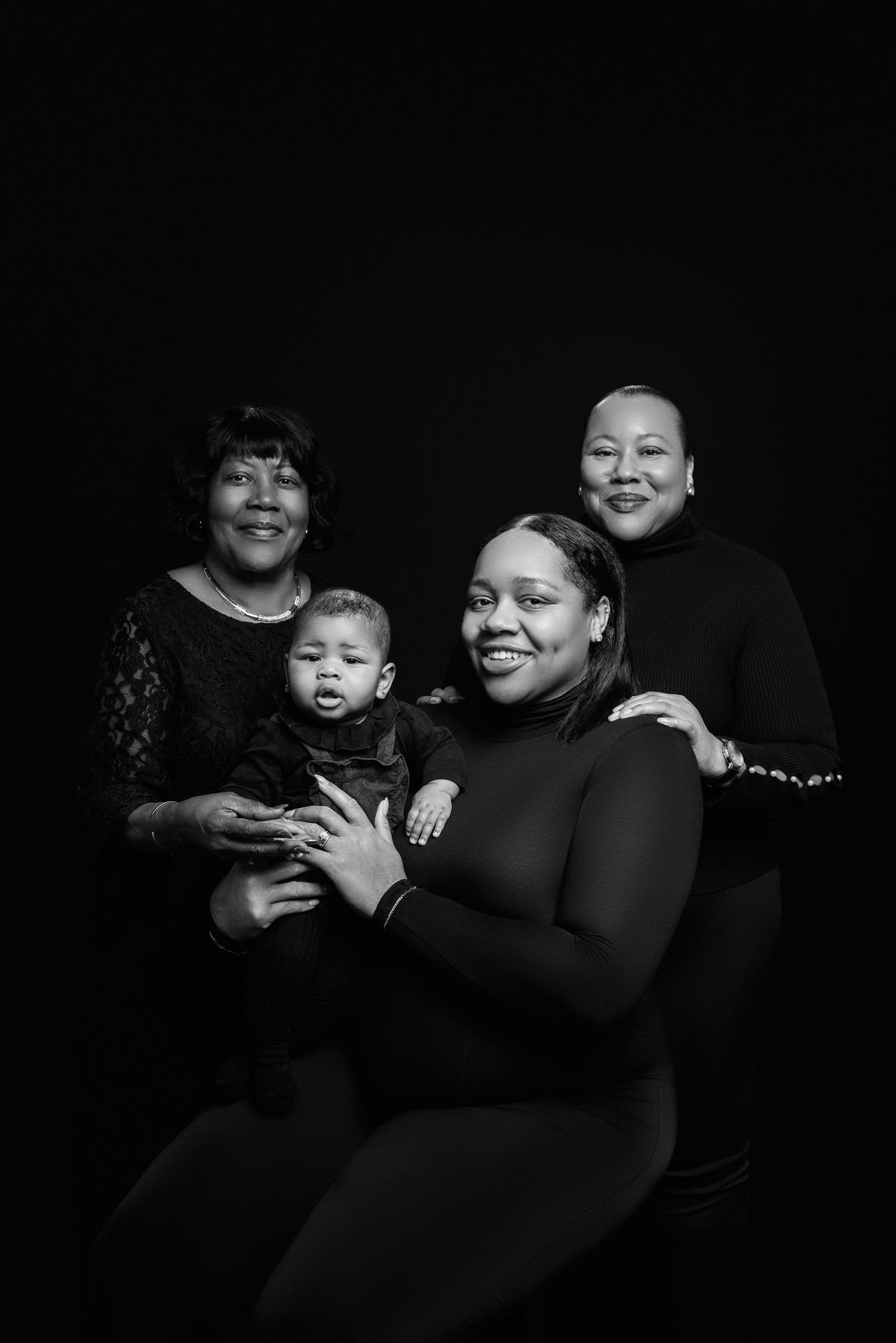 Black and white portrait of multi-generational family against dark background.