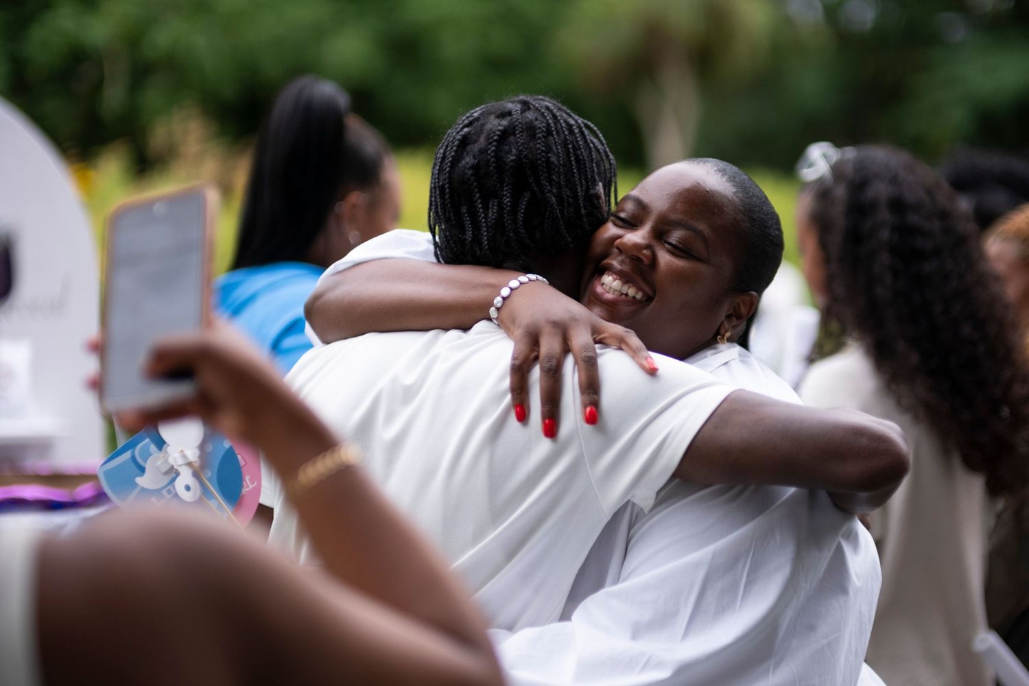 People dressed in white embracing and celebrating at an outdoor gathering.