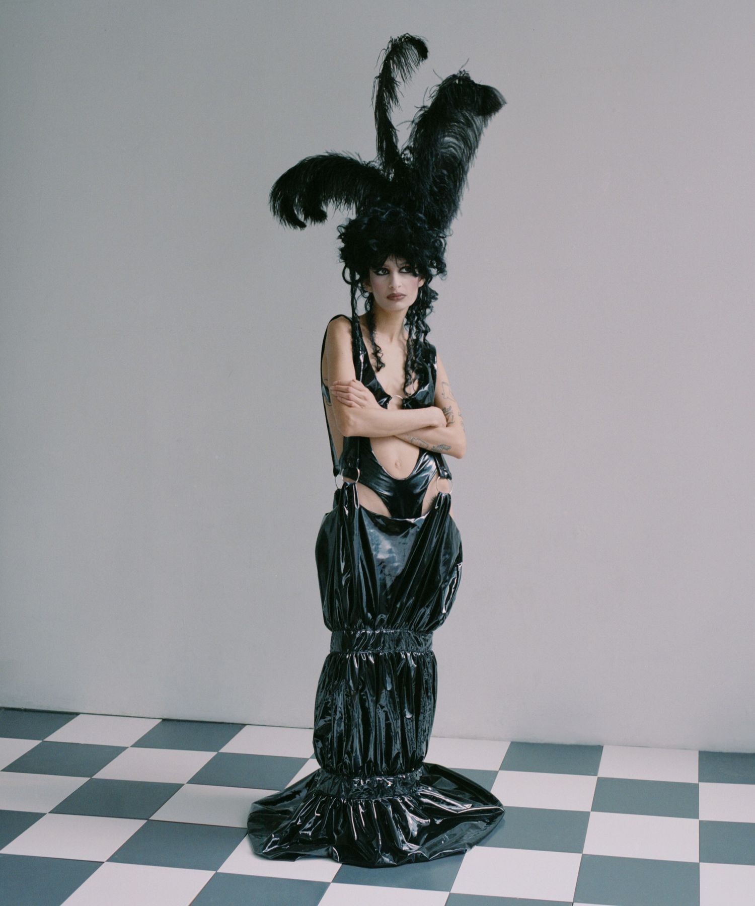 Model Biba stands on a black-and-white checkboard tile floor wearing a feather headpiece and a latex dress by a LaSalle college graduate.