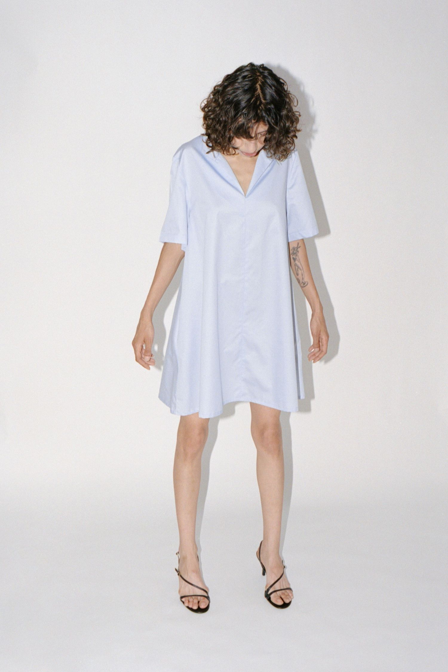 A wavy-haired brunette model wears a baby blue short cotton dress with by Canadian brand Waves of Hydra.