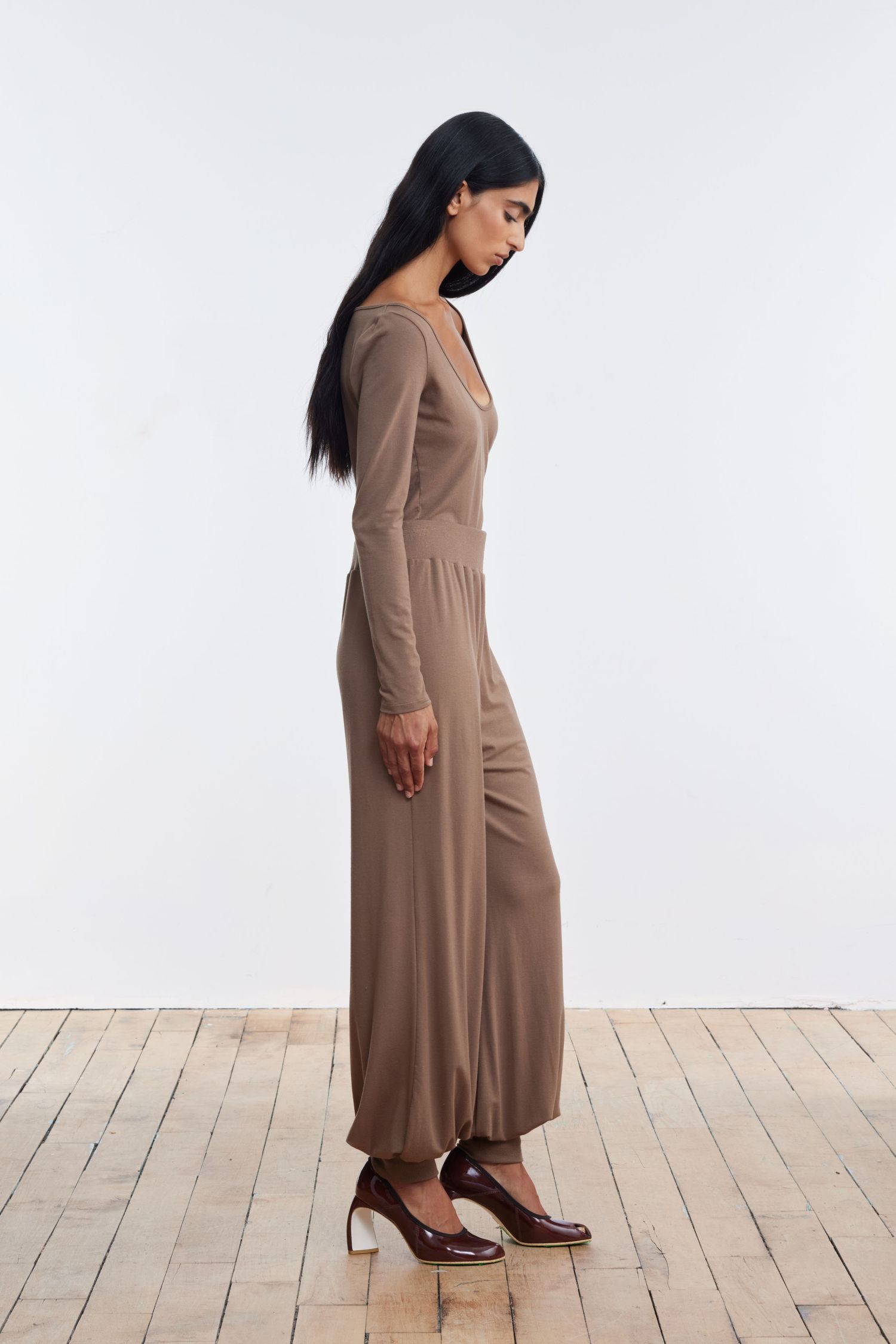 A model stands profile in studio wearing matching camel balloon pants and longsleeve scoop shirt.