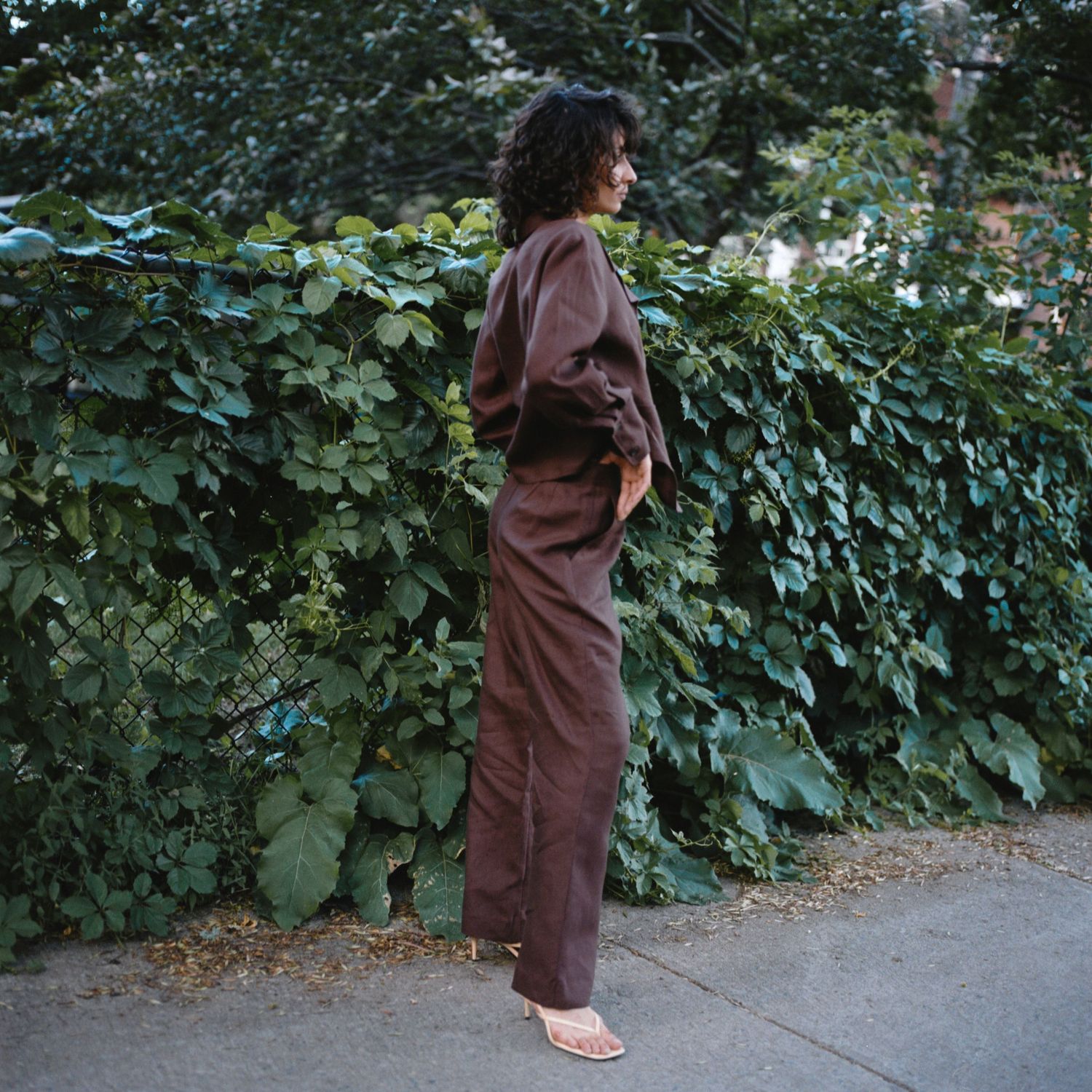 A woman with brown wavy hair wears a brown linen suit on a sidewalk in Montreal.