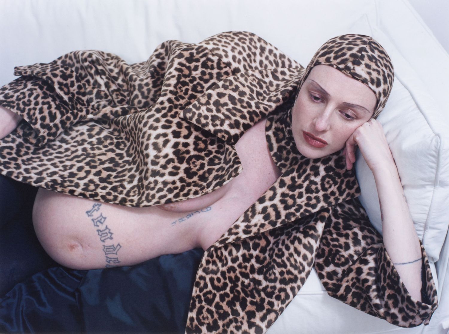 A pregnant model lounges on a couch wearing a leopard print coat and balaclava by designer Duran Lantink.