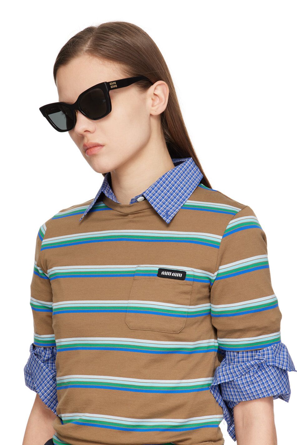 A model wears large black cateye sunglasses and a brown and green striped top by Miu Miu.
