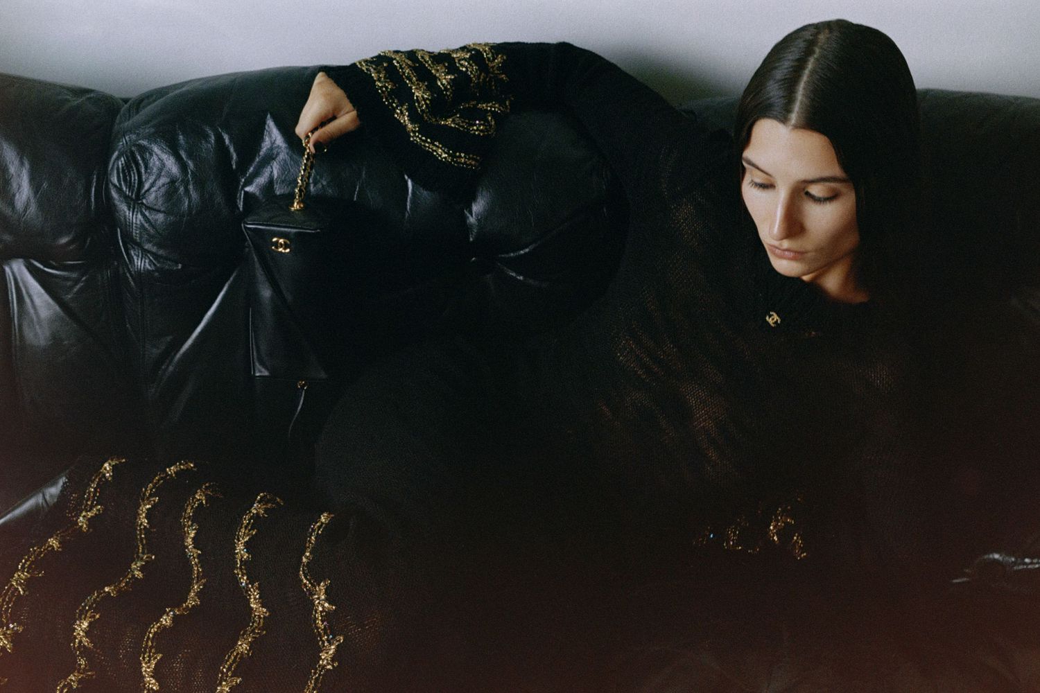 Influencer Andrea Ricci lounges on a black leather couch at Montréal's Maison Singulier while wearing Chanel Métiers d'arts '24/25.