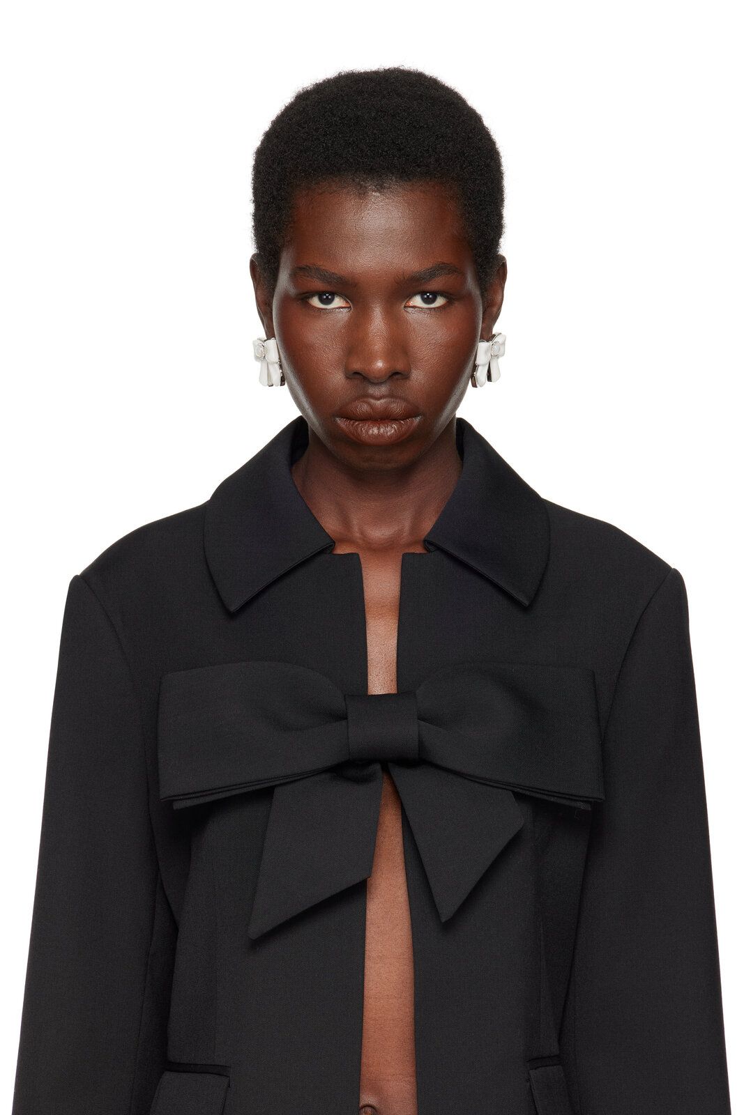A model wears SHUSHU/TONG black suit blazer featuring a detachable bow appliqué at the open front