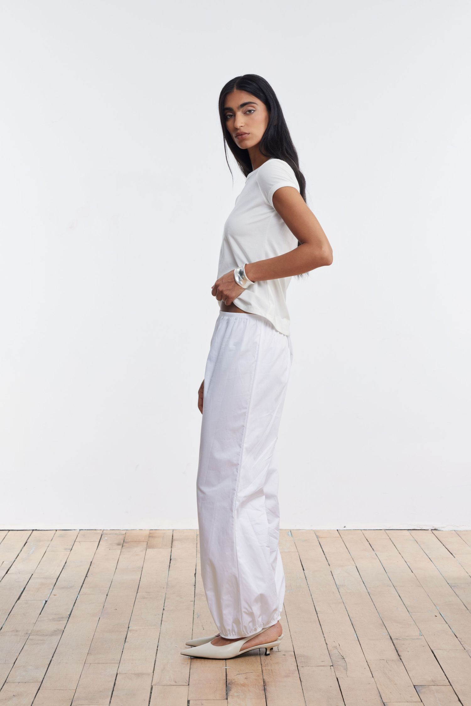 A model stands profile looking at the camera wearing white cotton balloon pants and a white jersey tee.