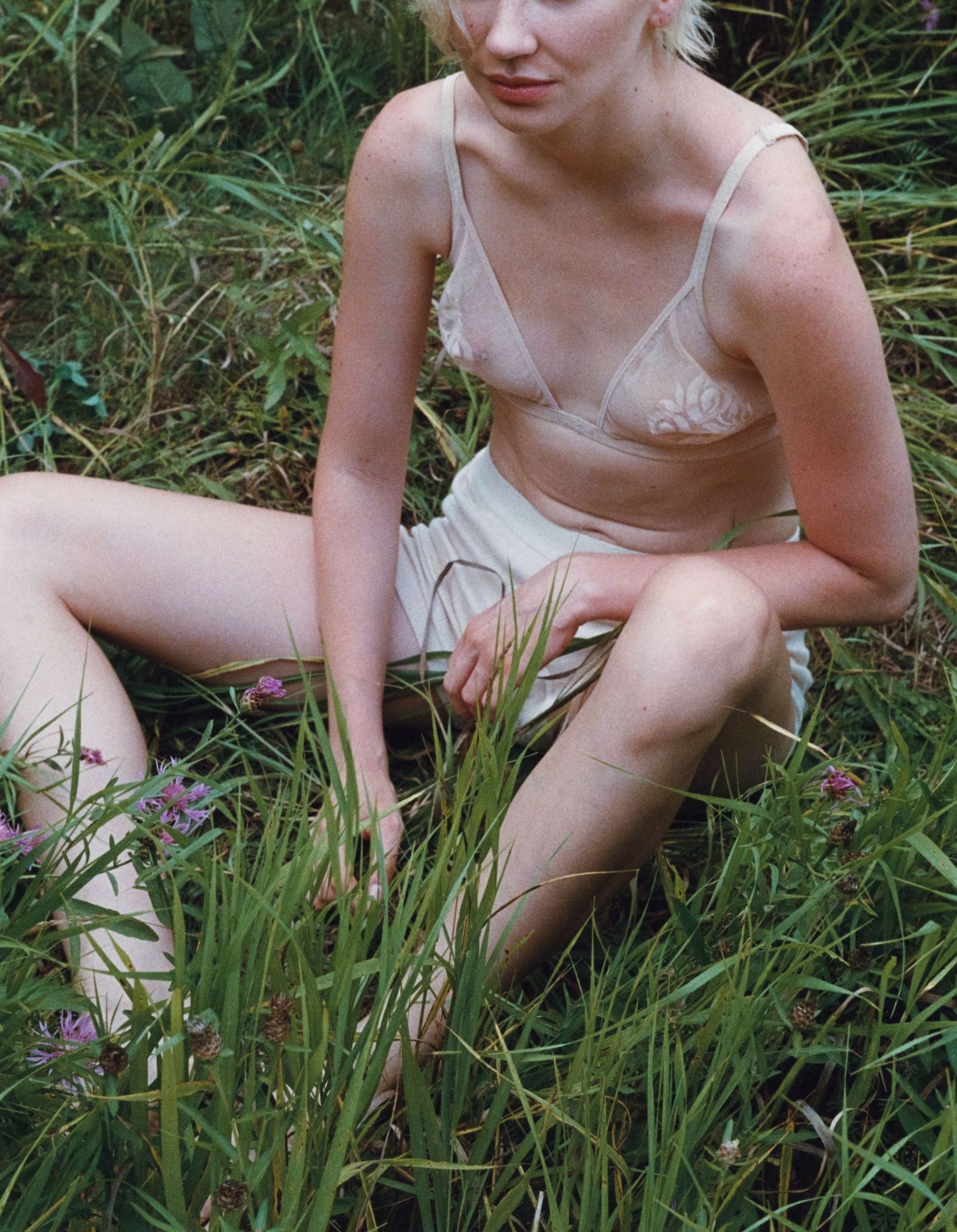 Editorial portrait photographed on film featuring a model seated in tall grass wearing sheer cream vintage undergarments.