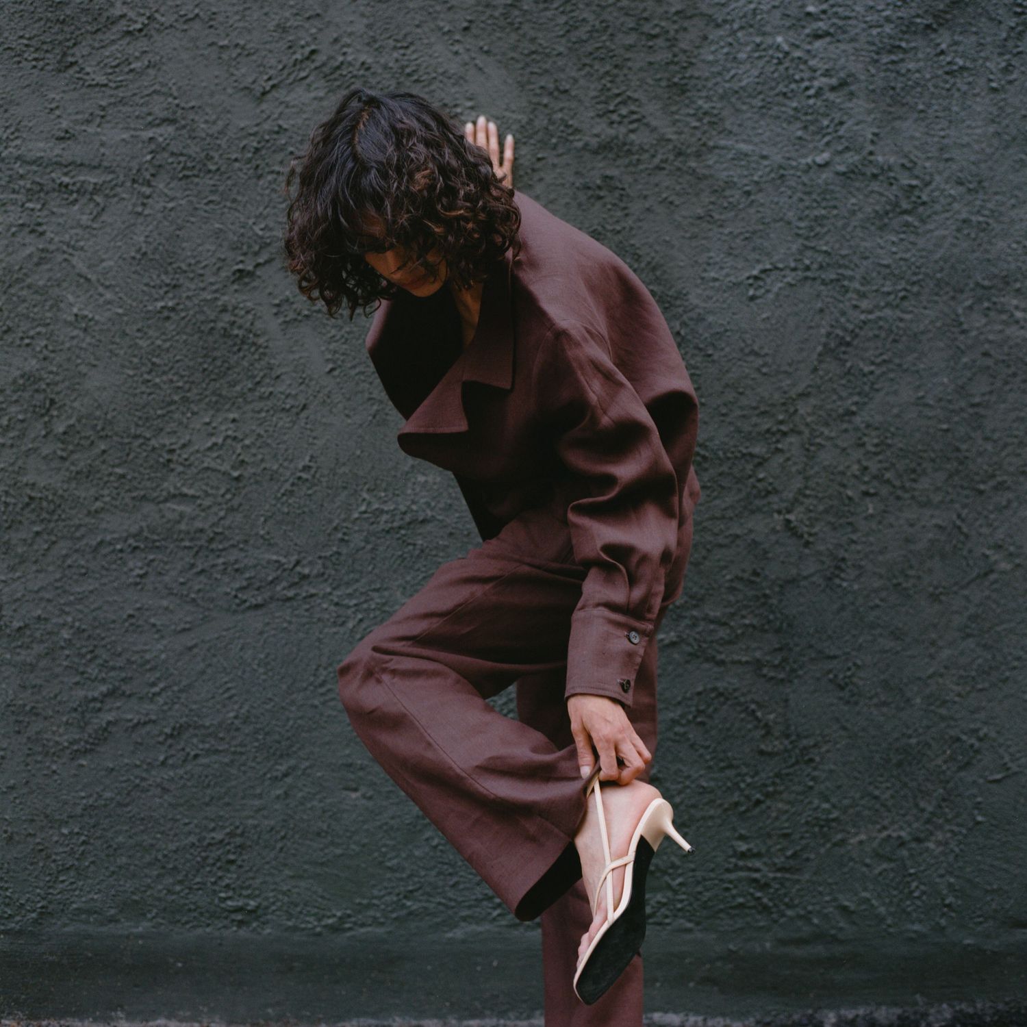 A model adjusts her strappy shoe while wearing a brown linen suit from Waves of Hydra.