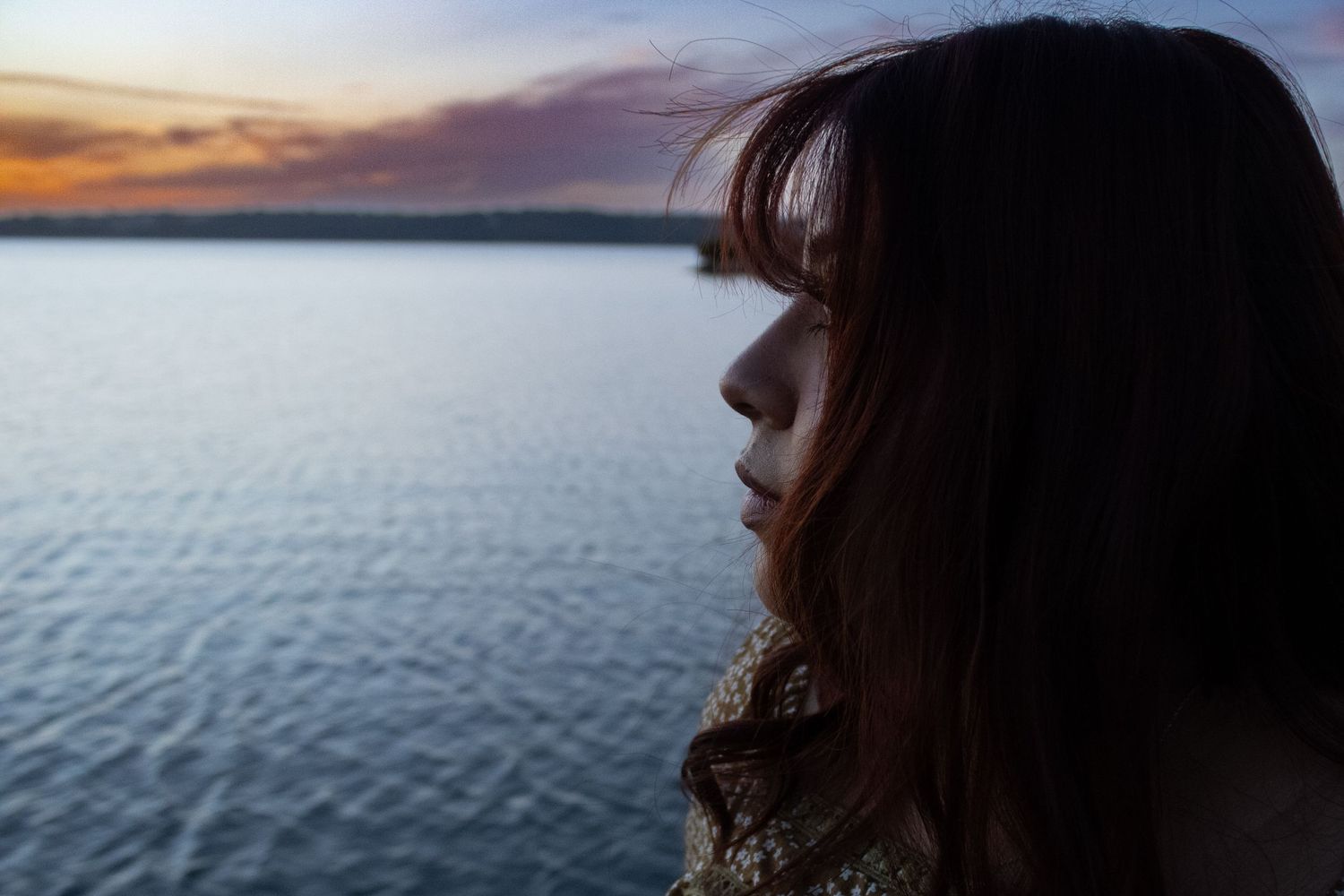 Close-up portrait of woman looking over the water at sunset