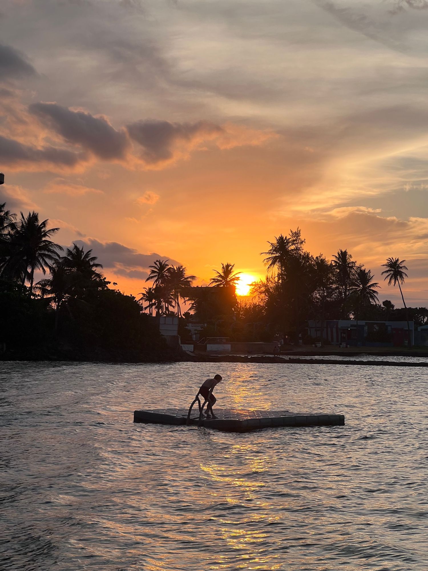 Person on a landing pad on the water beneath a colorful sunset sky