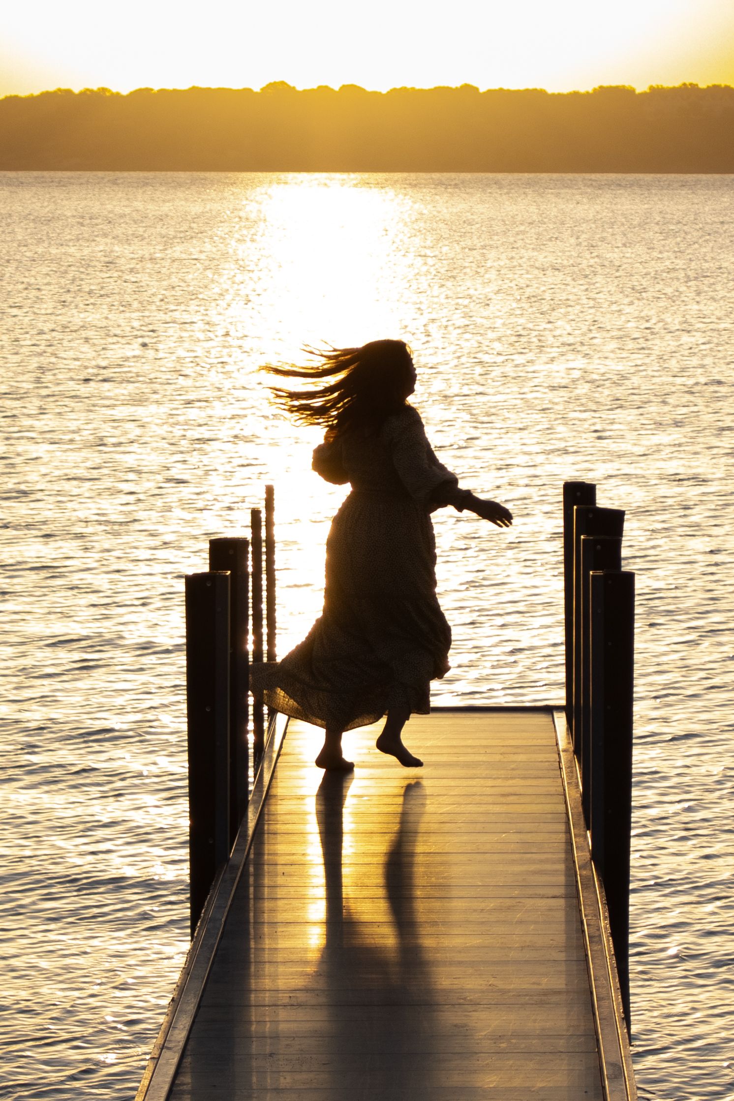 Woman walking on a dock silhouetted by golden sunset light
