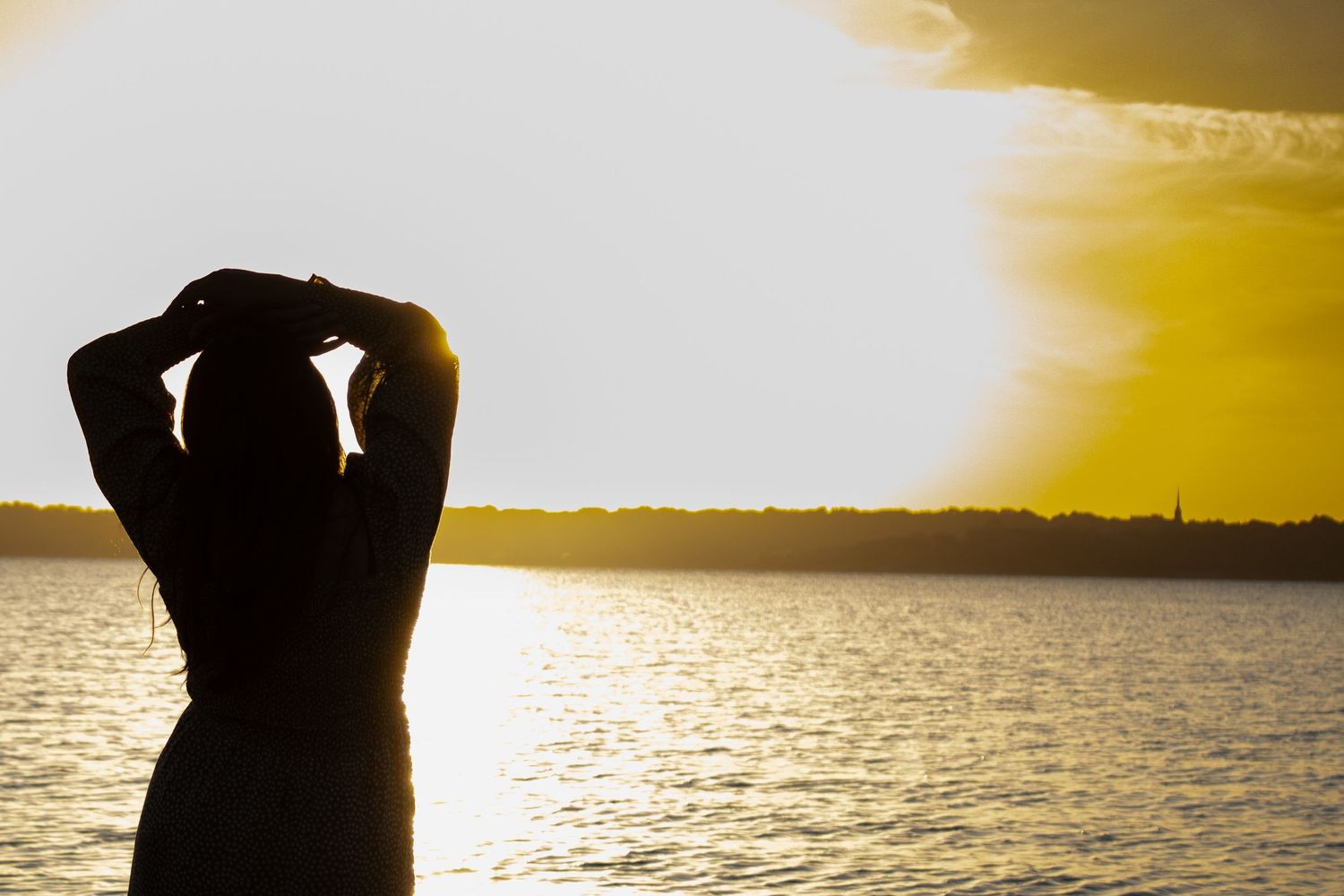 Silhouette of a woman posing against a golden sunset over the water