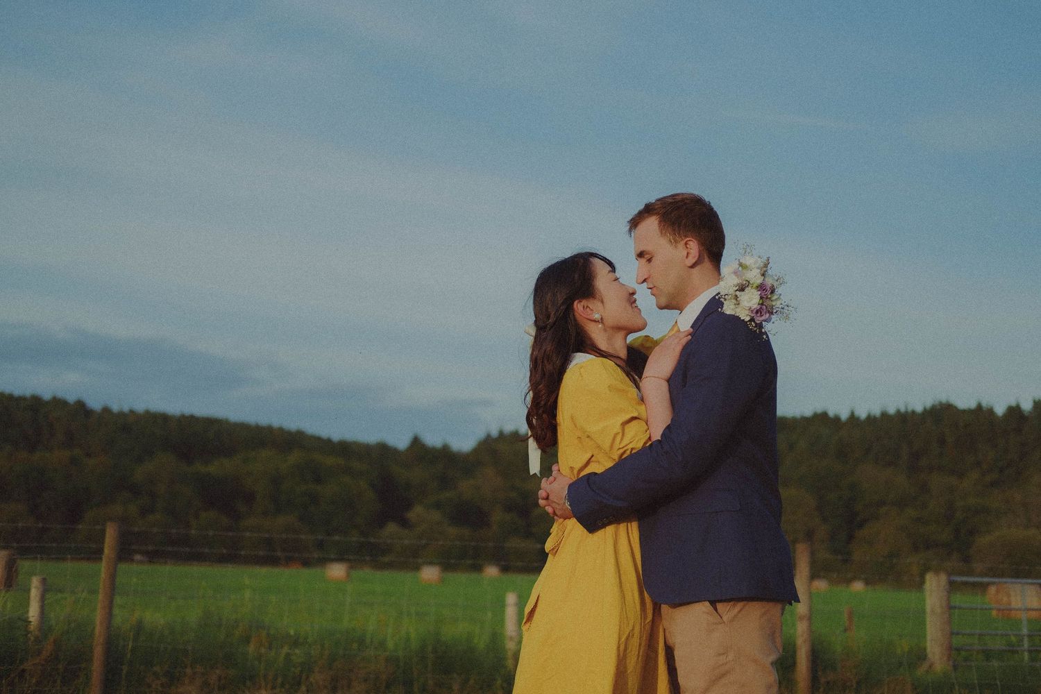 Romantic pre-wedding photograph of a couple embracing in an open field, surrounded by the countryside.