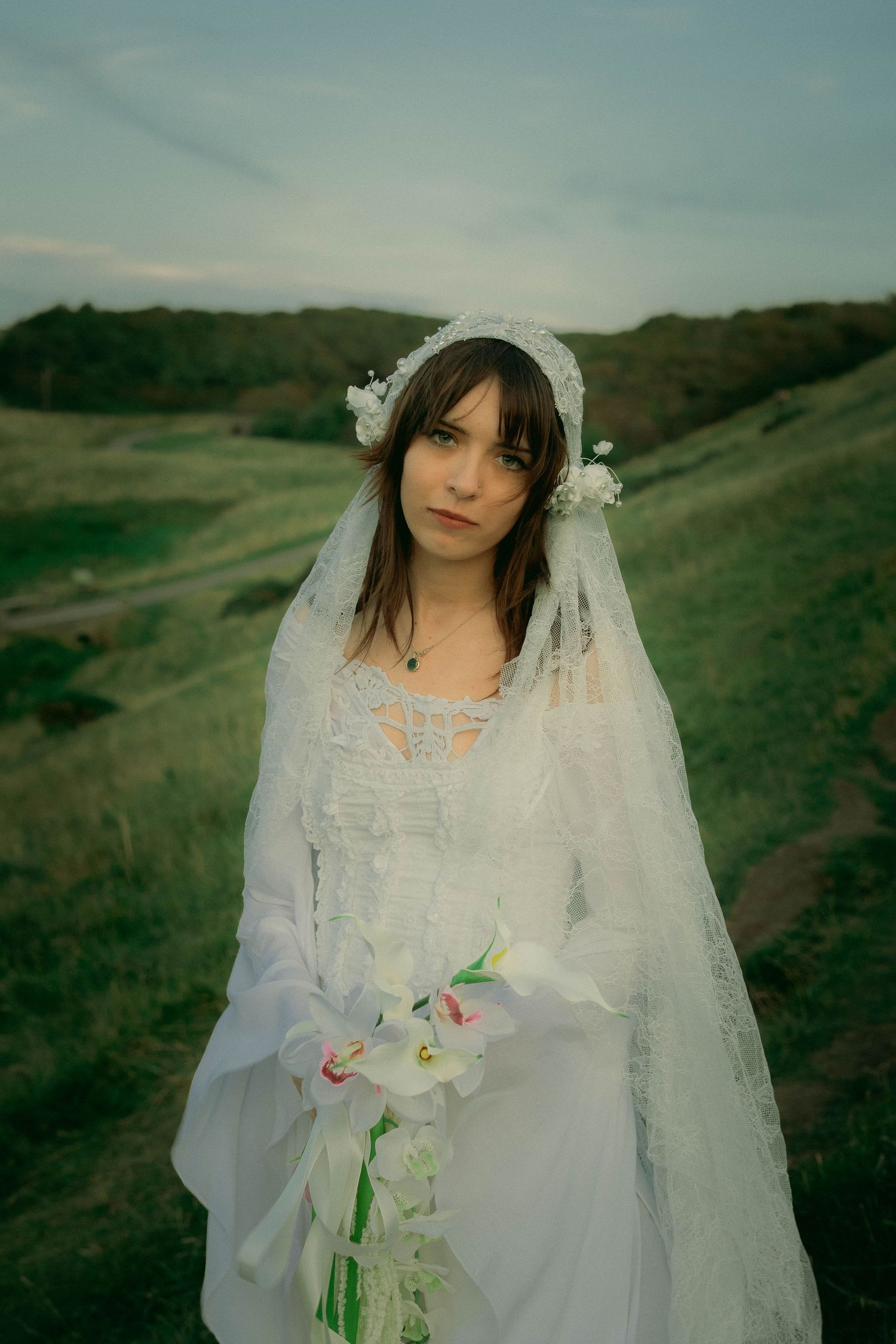 A portrait of a newlywed bride standing outdoor in a country side looking at the camera.