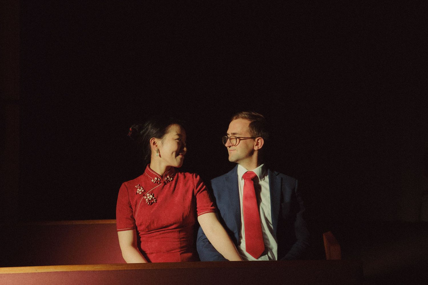 Intimate couples photograph of a couple sitting together in a cinema, sharing a quiet moment under warm cinematic lighting.